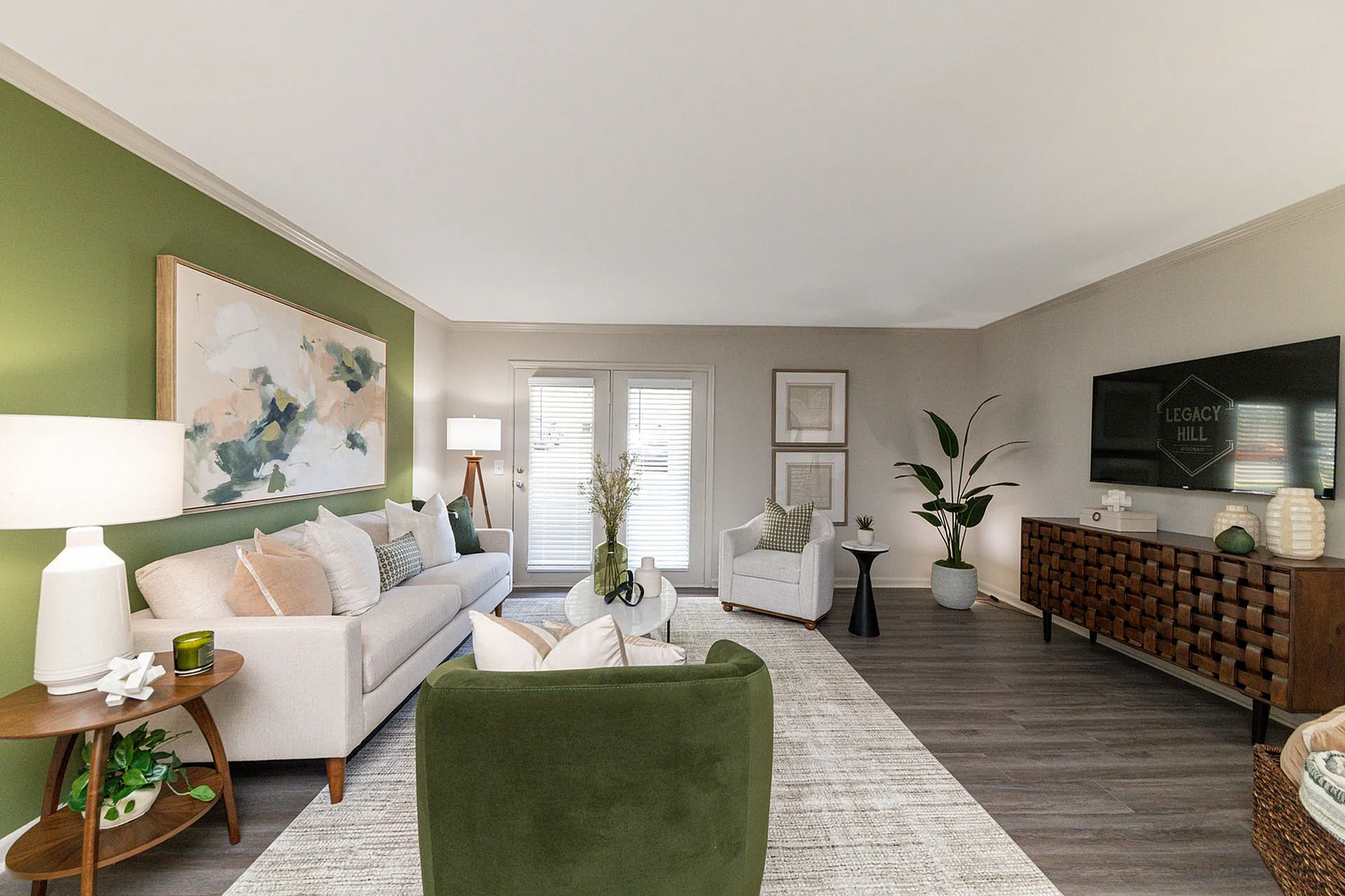 Chic living room with modern decor, featuring a cozy sofa against a green accent wall, stylish furniture, and abundant natural light.