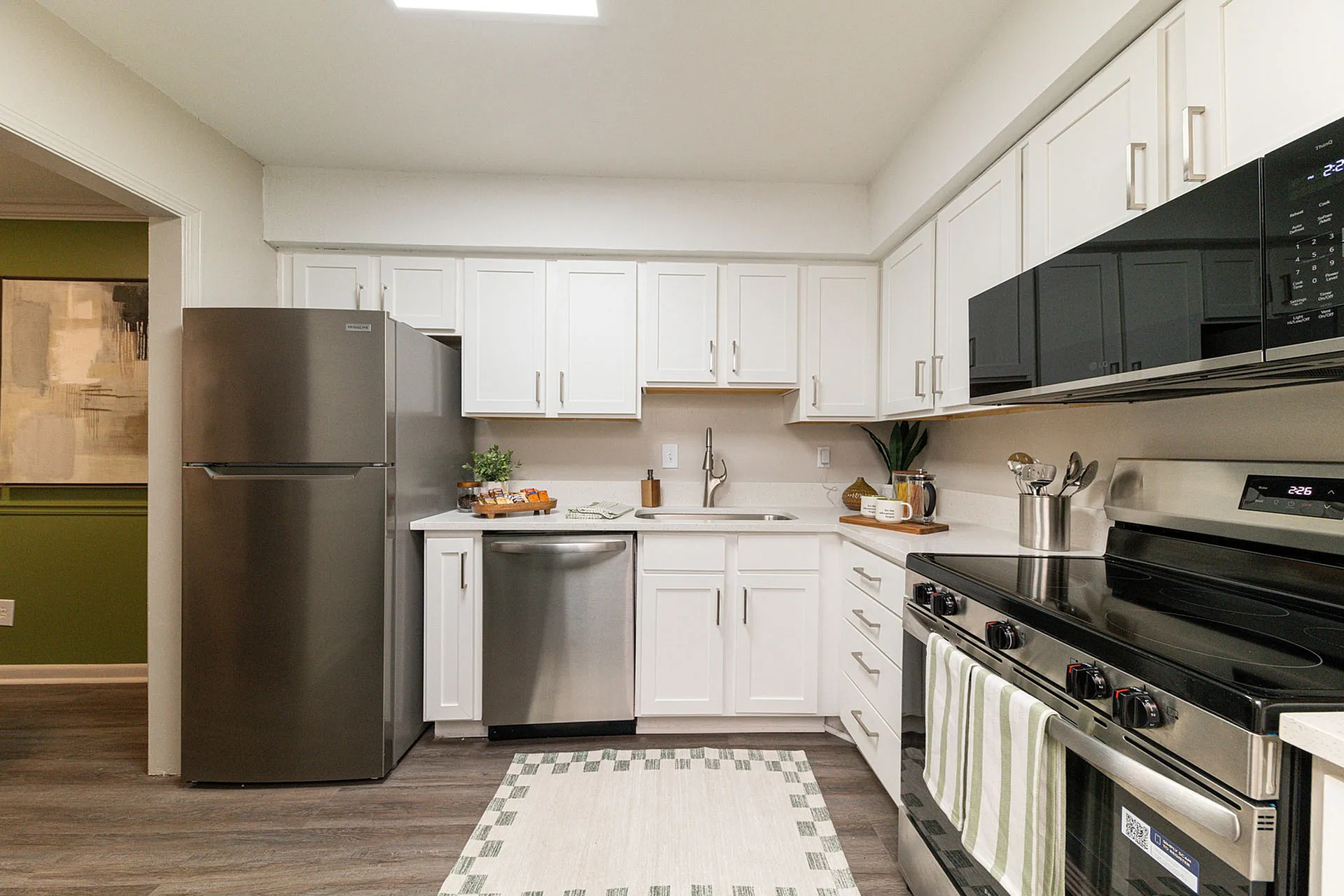 Modern kitchen with sleek stainless steel appliances, pristine white cabinets, and stylish wood flooring.