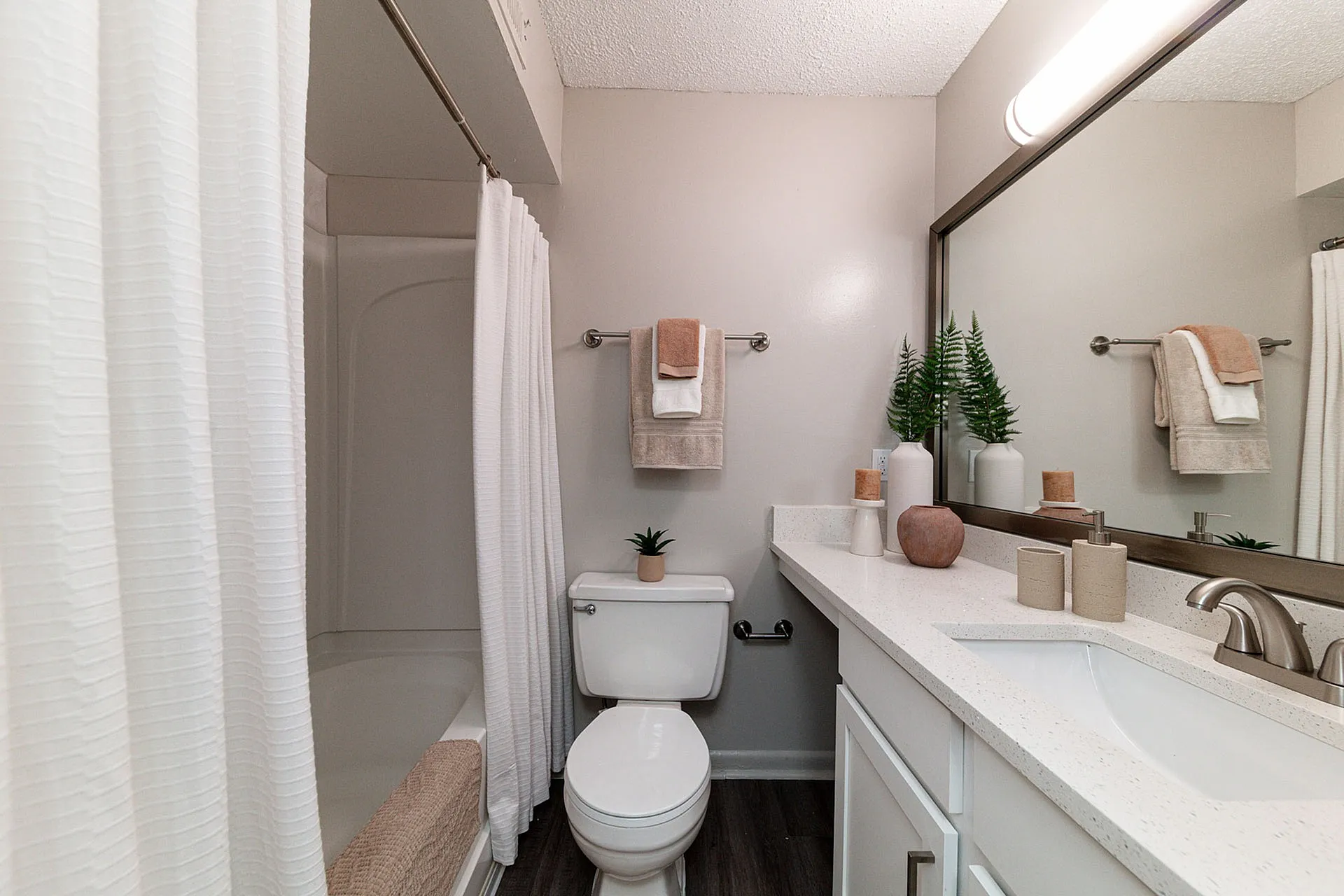 Modern bathroom with sleek white cabinetry, elegant countertop decor, and a tranquil bathtub with a privacy curtain.