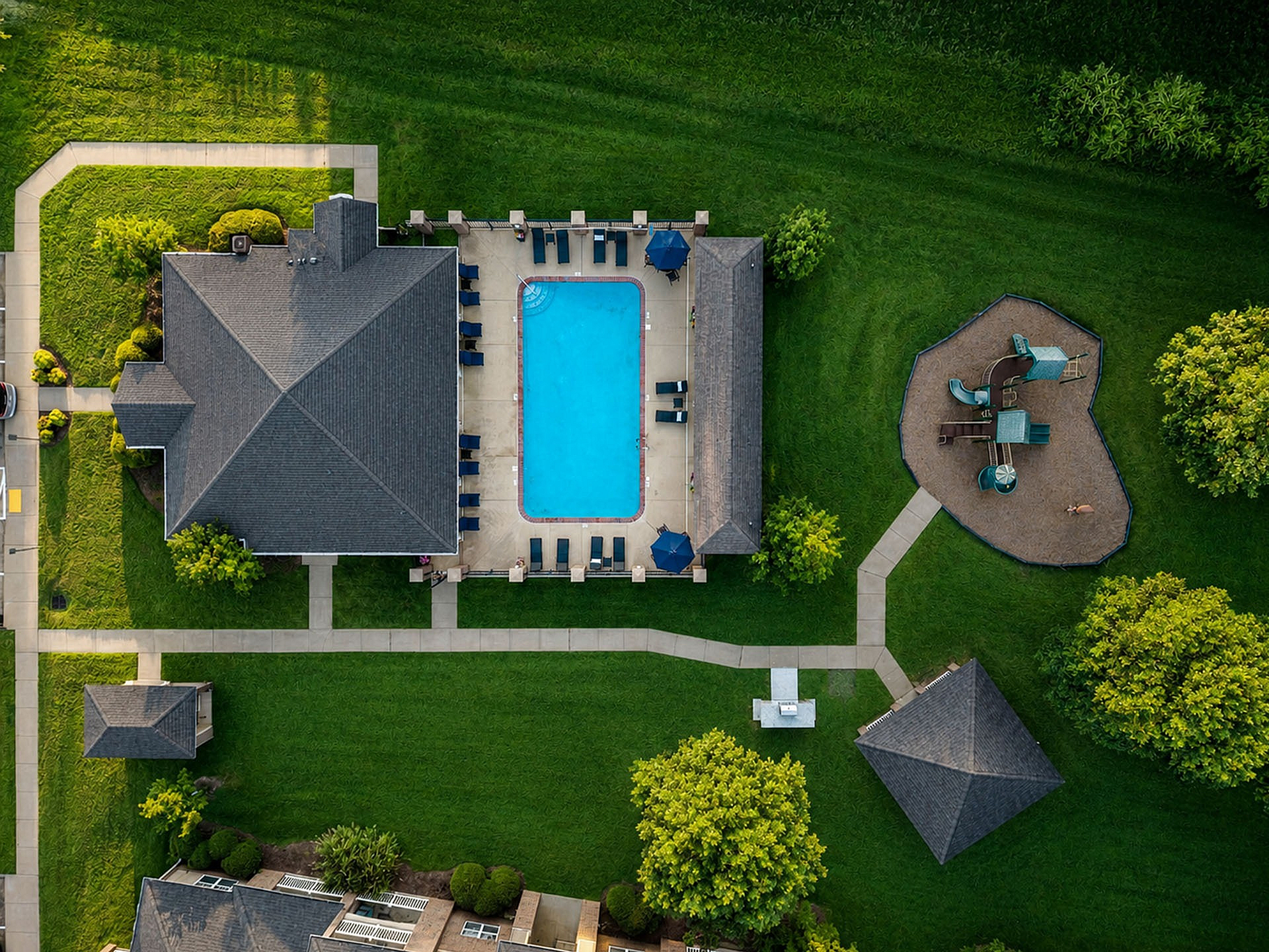 Stunning aerial view of a luxurious apartment complex featuring a sparkling pool with sun loungers, surrounded by lush greenery and a charming playground.