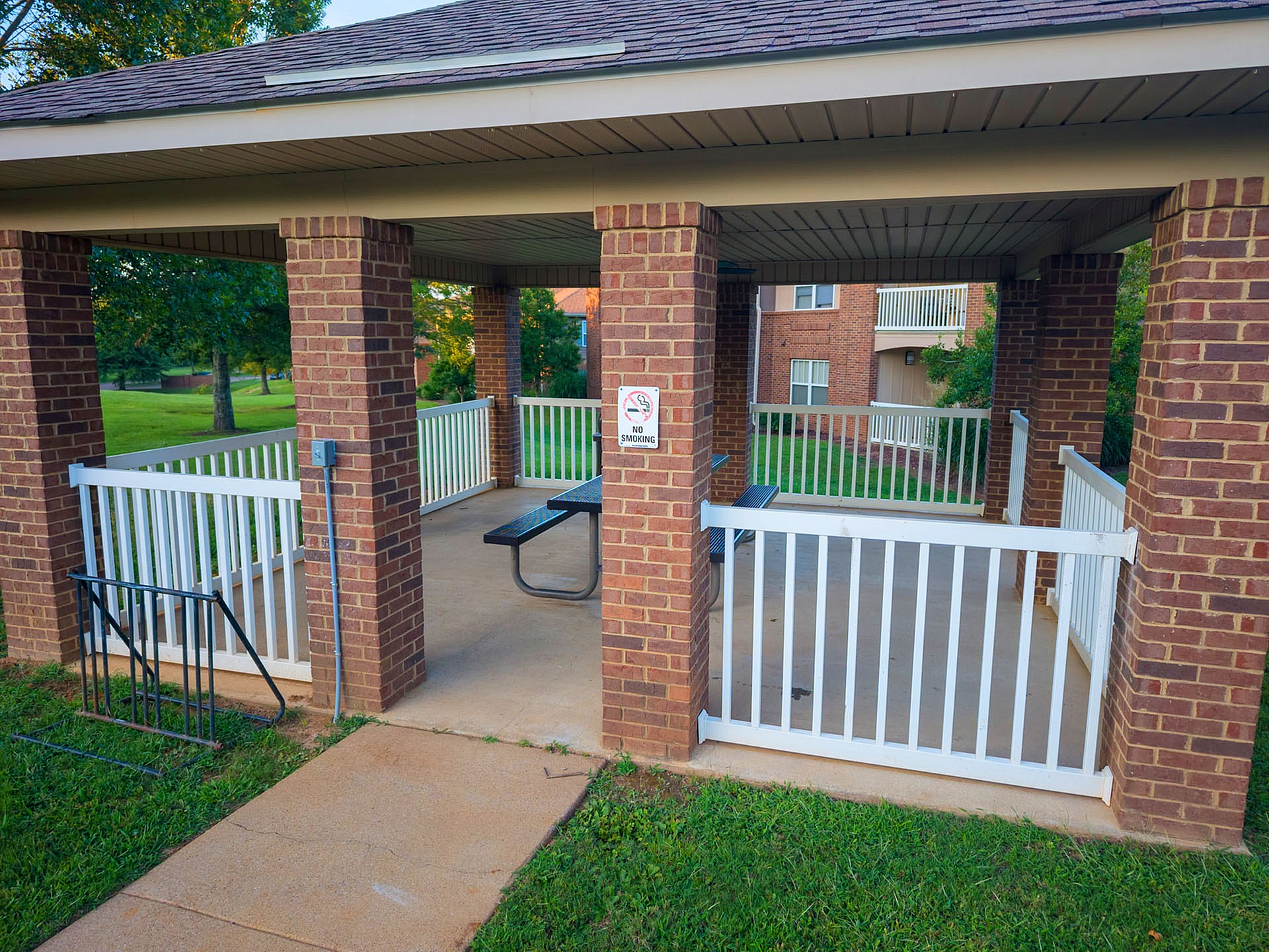 Inviting outdoor brick pavilion with picnic table, perfect for leisure and community gatherings in a lush green setting.