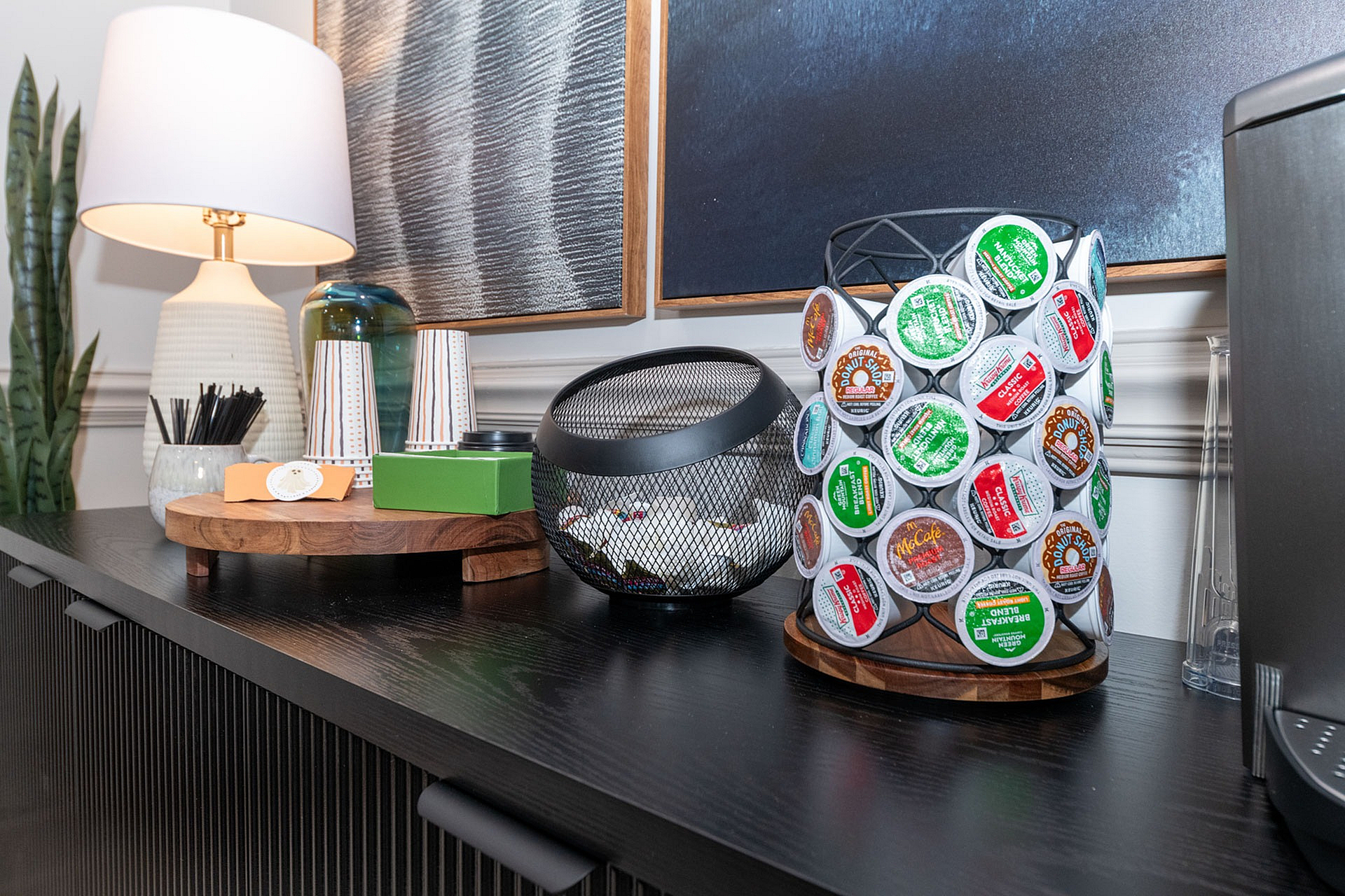 Elegant coffee station with a sleek black counter, stylish lamp, coffee pods, and modern decor accents for a welcoming ambiance.