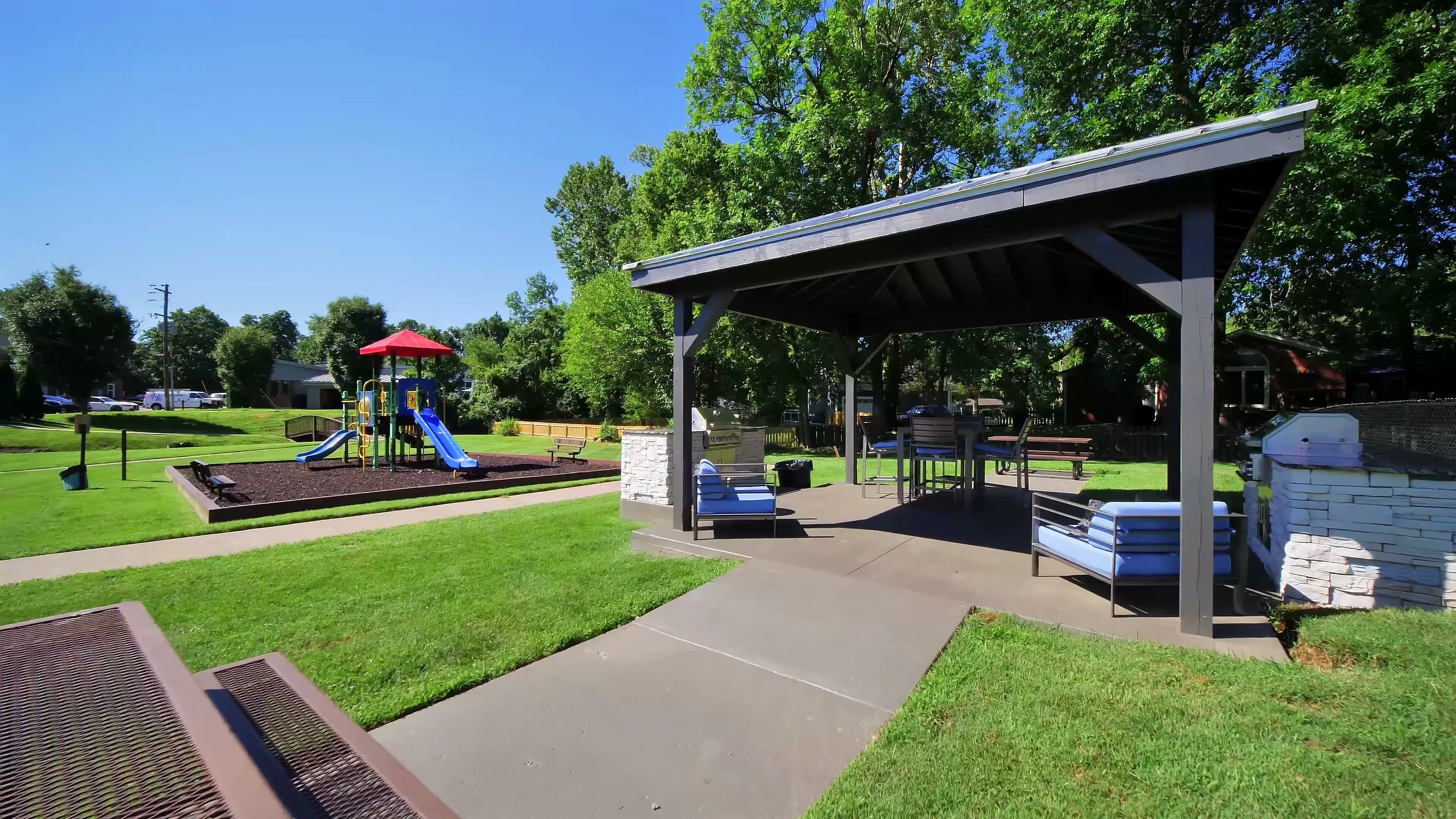 Inviting outdoor recreation area featuring a covered pavilion with seating, adjacent to a colorful playground set amid lush greenery.