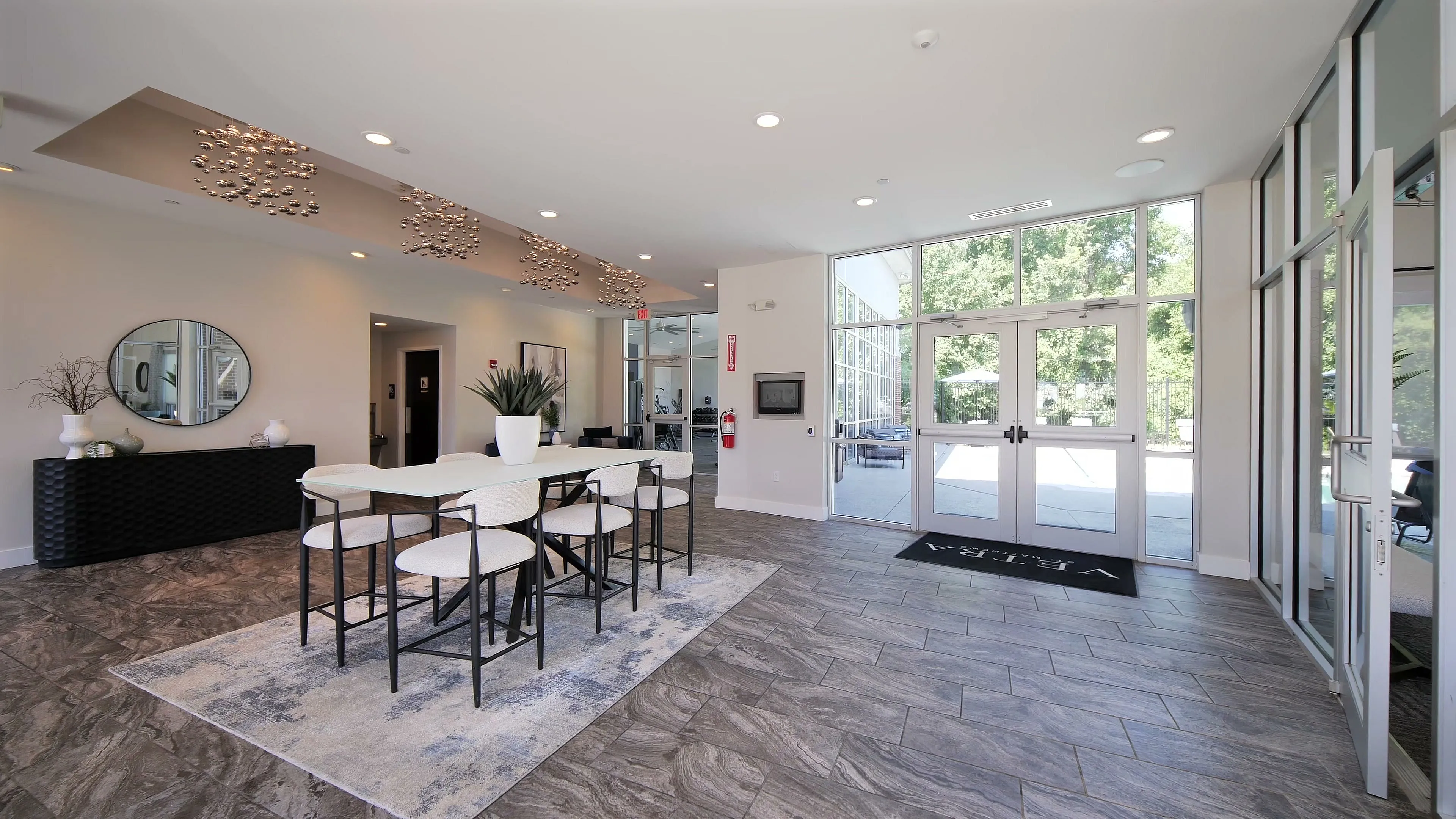 Bright and modern apartment lobby with elegant decor, large windows, and contemporary lighting fixtures.