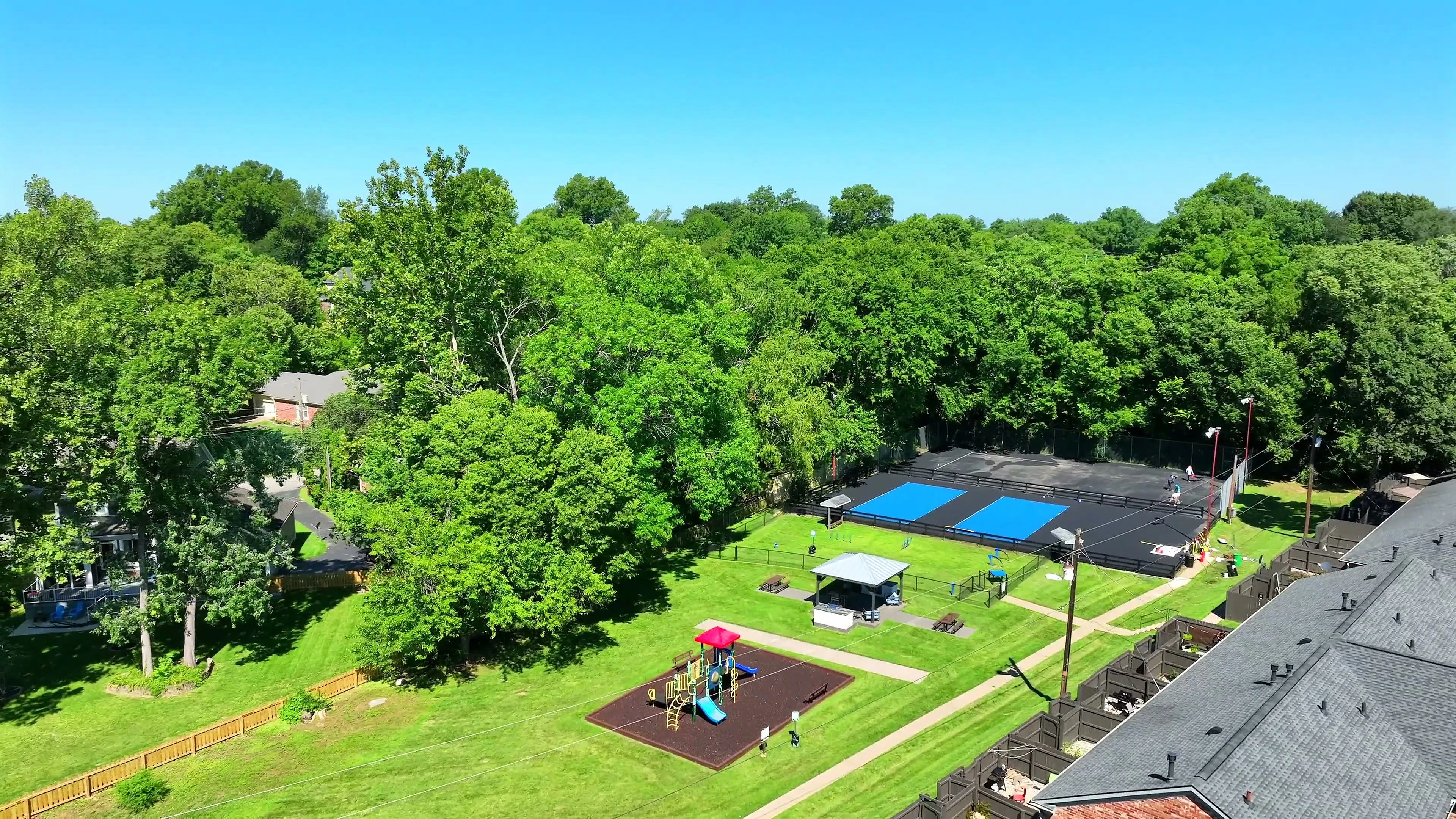 Scenic aerial view of lush green spaces with a vibrant playground and modern tennis courts, perfect for family recreation and active living.