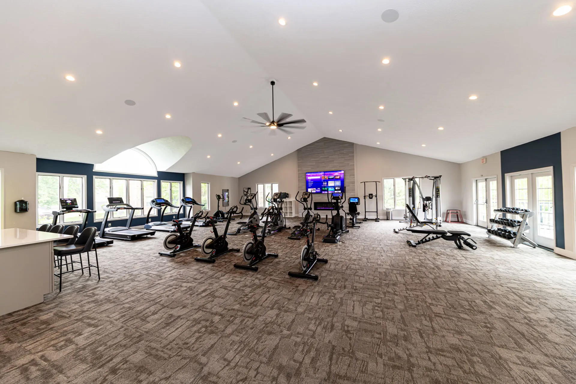 Spacious and modern fitness center with high ceilings, featuring treadmills, exercise bikes, and strength training equipment, all bathed in natural light.