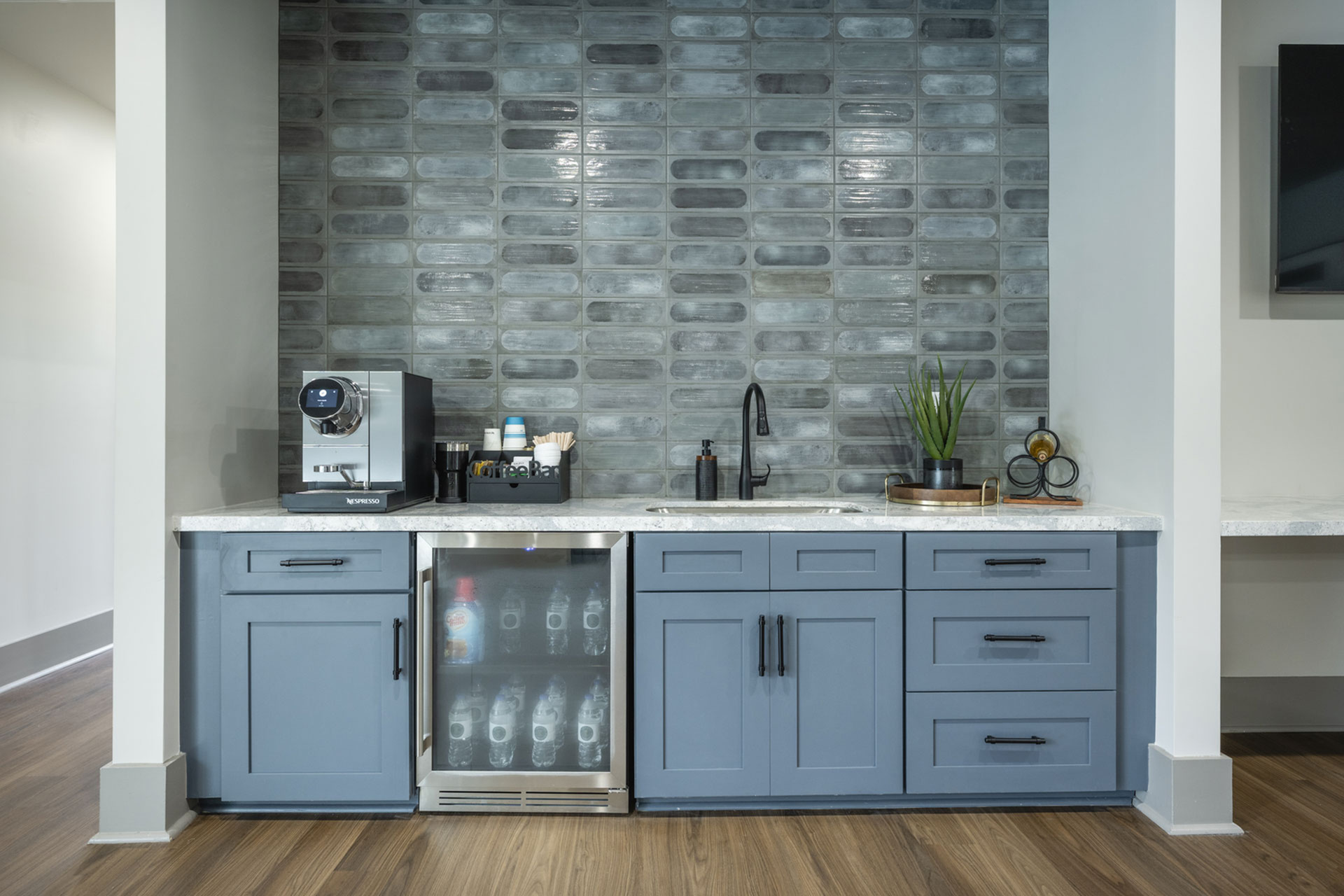 Contemporary kitchen area with sleek blue cabinetry, a modern coffee machine, and a stylish tile backsplash, perfect for a chic apartment lifestyle.