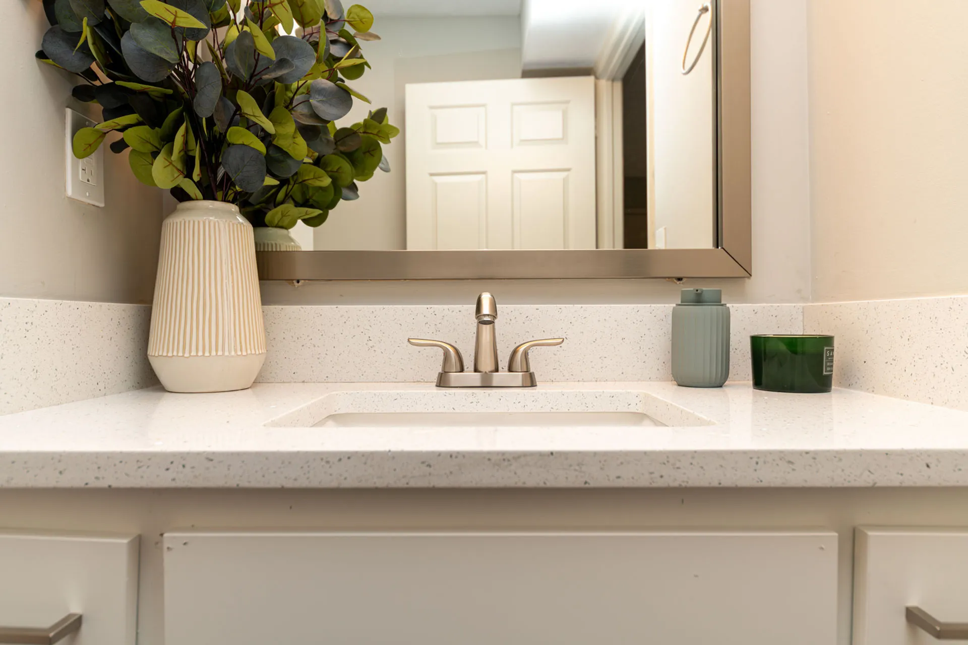 Elegant bathroom vanity featuring a sleek faucet, modern speckled countertop, and stylish vase with lush greenery.