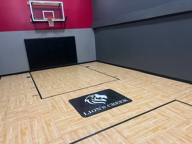 Modern indoor basketball court at Lion\'s Creek with sleek wooden flooring and vibrant red and gray walls.