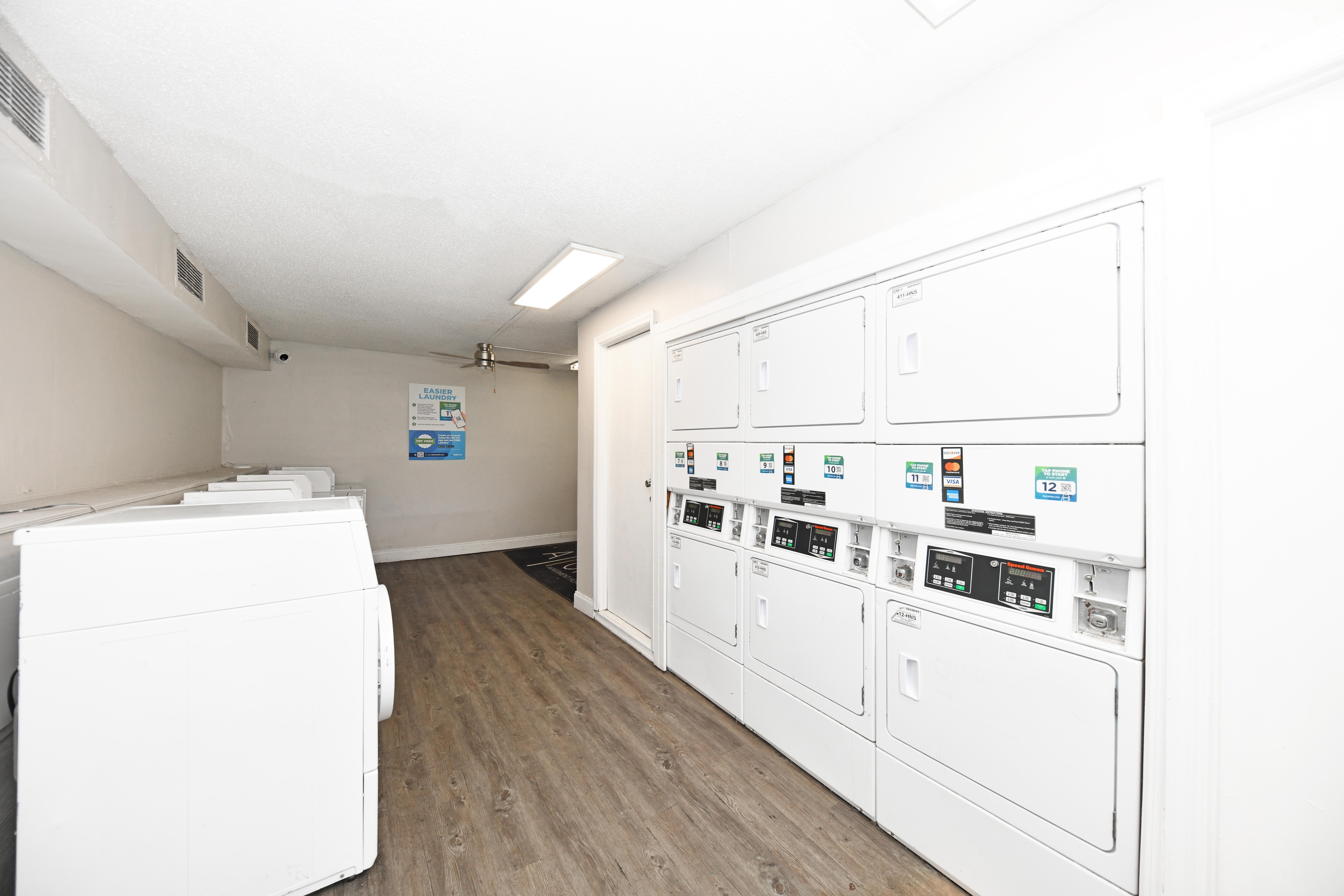 Modern laundry room with multiple washers and dryers, featuring sleek white machines and wood floors, offering convenience and style.