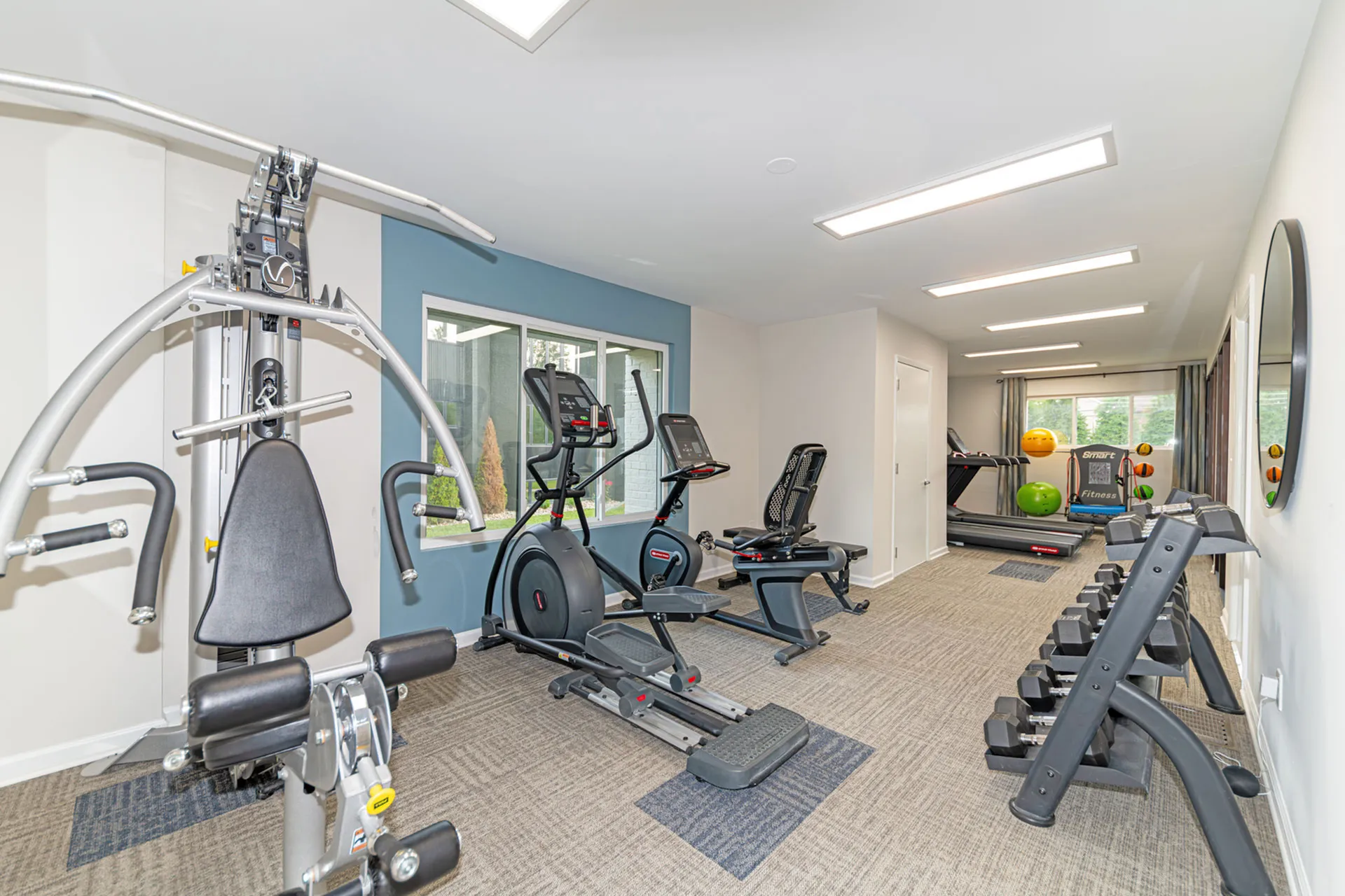 Modern fitness center with state-of-the-art exercise equipment, free weights, and ample natural light in a spacious, bright setting.
