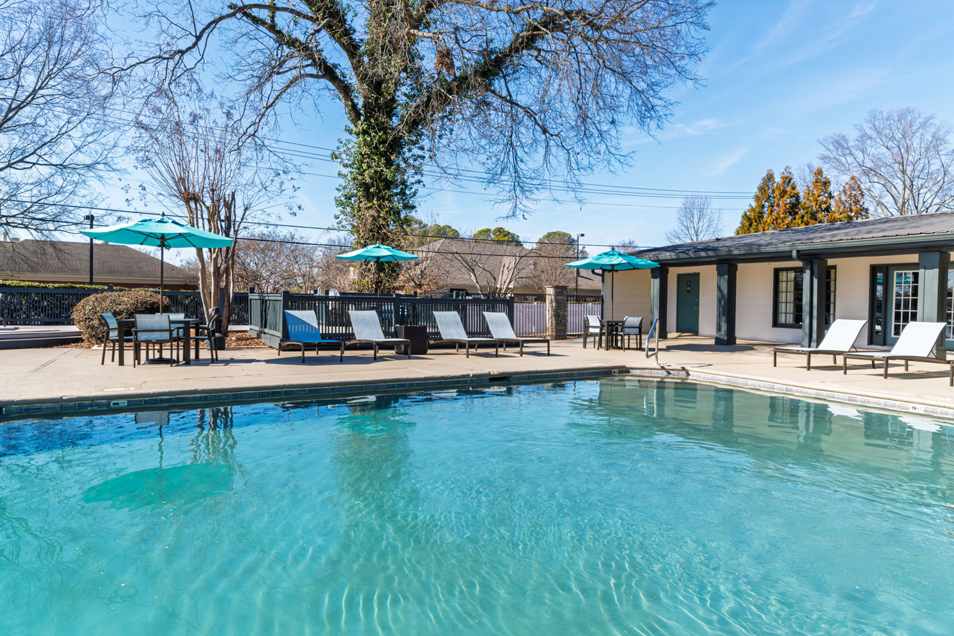 Inviting outdoor pool area with luxurious lounge chairs and chic umbrellas, surrounded by lush trees and modern architecture.