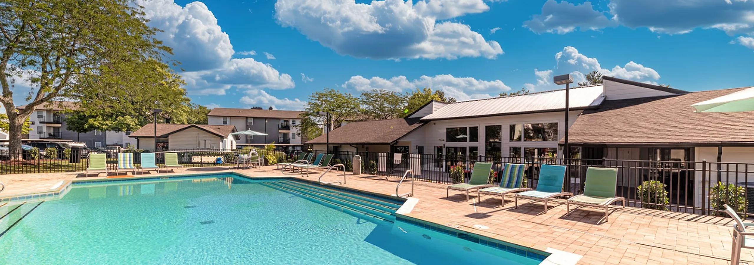 Inviting swimming pool surrounded by lounge chairs and a modern clubhouse under a clear blue sky.