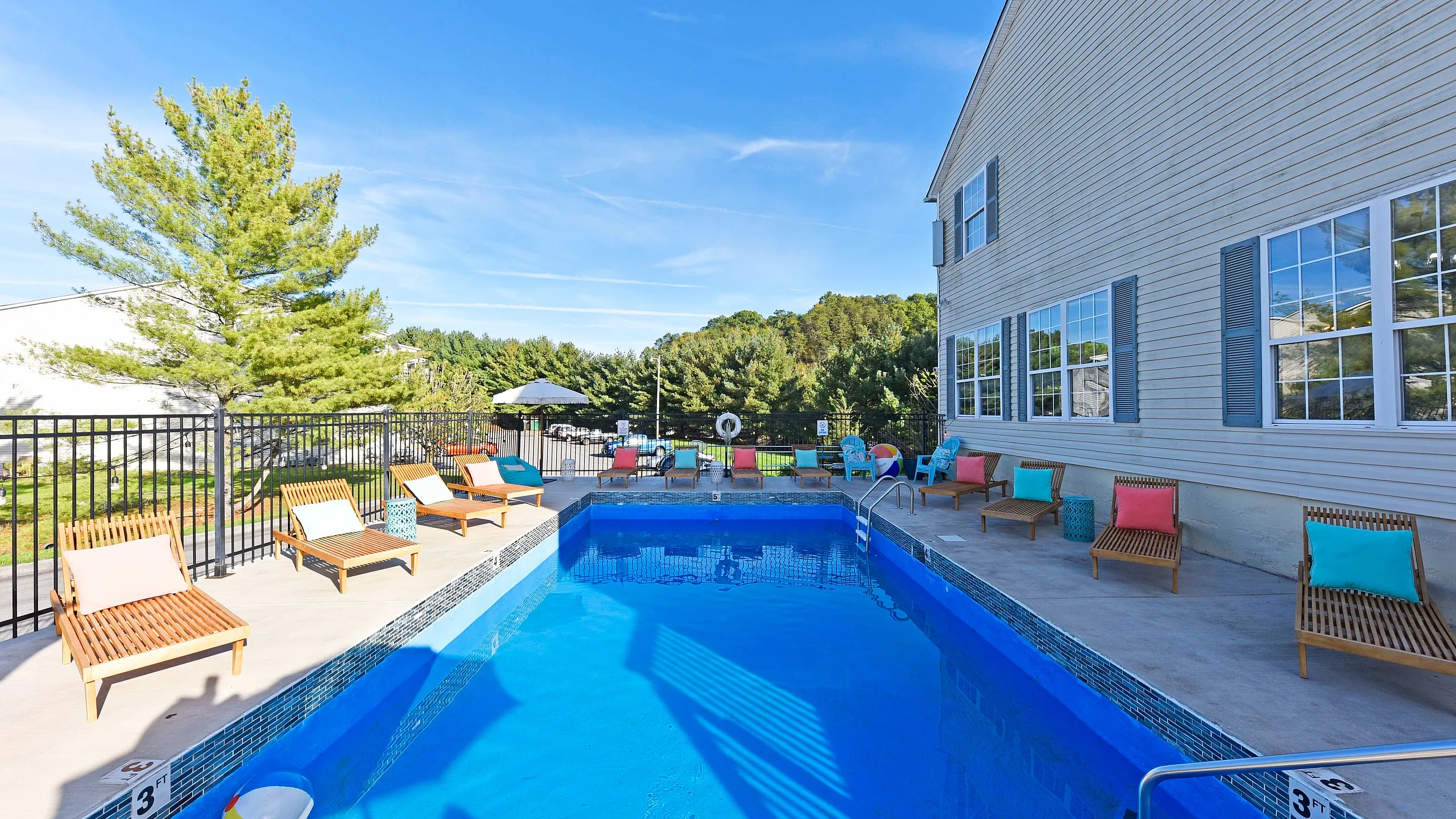 A serene outdoor pool area with comfortable lounge chairs and clear blue water, surrounded by lush greenery.