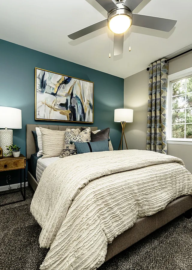 Elegant bedroom with modern decor, featuring a comfortable bed, stylish lamps, blue accent wall, and large window with curtains.