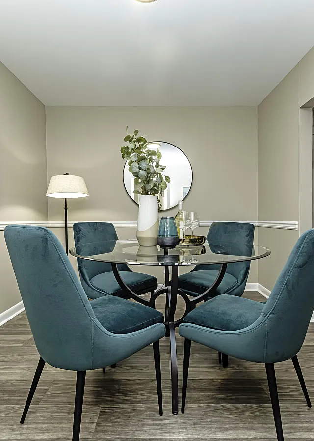 Stylish dining area with modern glass table and teal velvet chairs, accentuated by contemporary artwork and elegant decor.