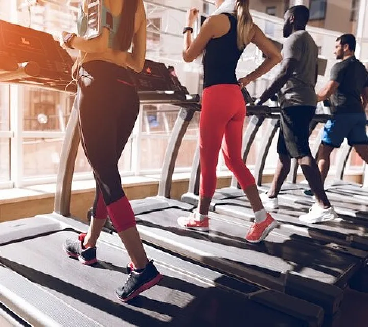 Group of individuals running on treadmills in a well-lit modern fitness center.