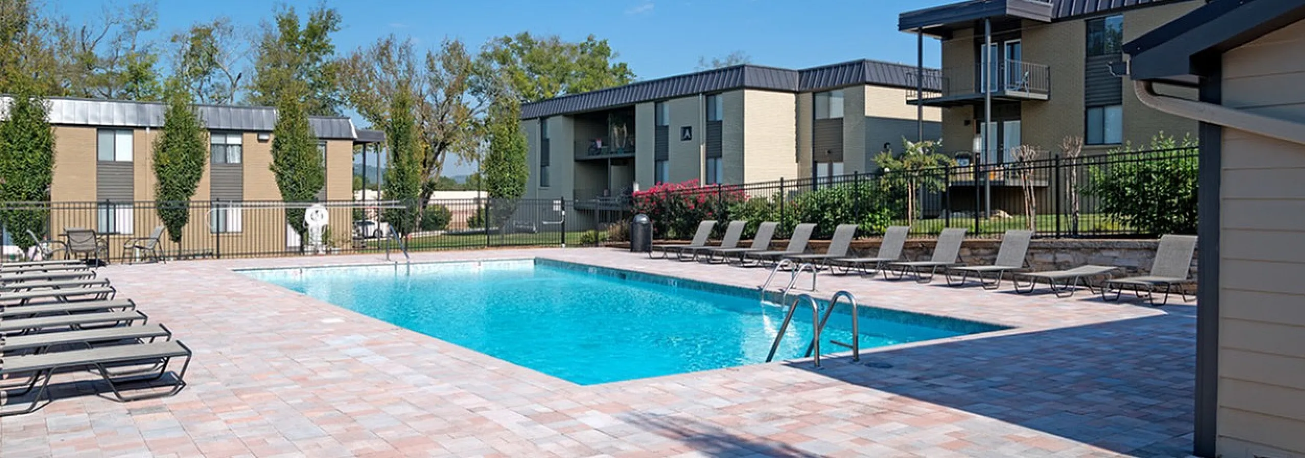 Charming apartment complex with a sparkling outdoor pool and lounging chairs under a clear blue sky.