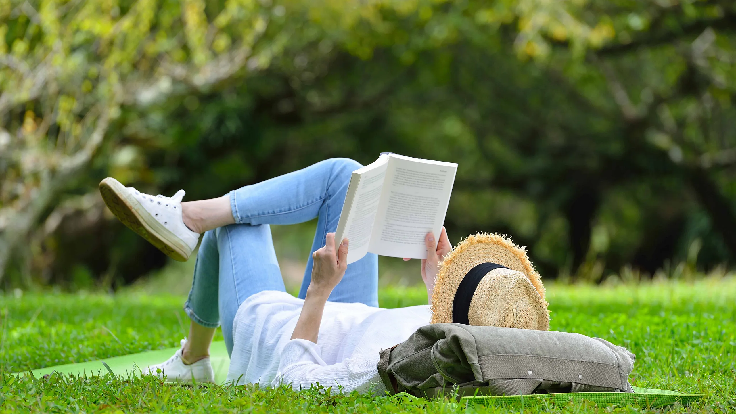 Relaxing outdoor scene with a person lying on the grass, reading a book in a tranquil park setting, perfect for leisure and unwinding.