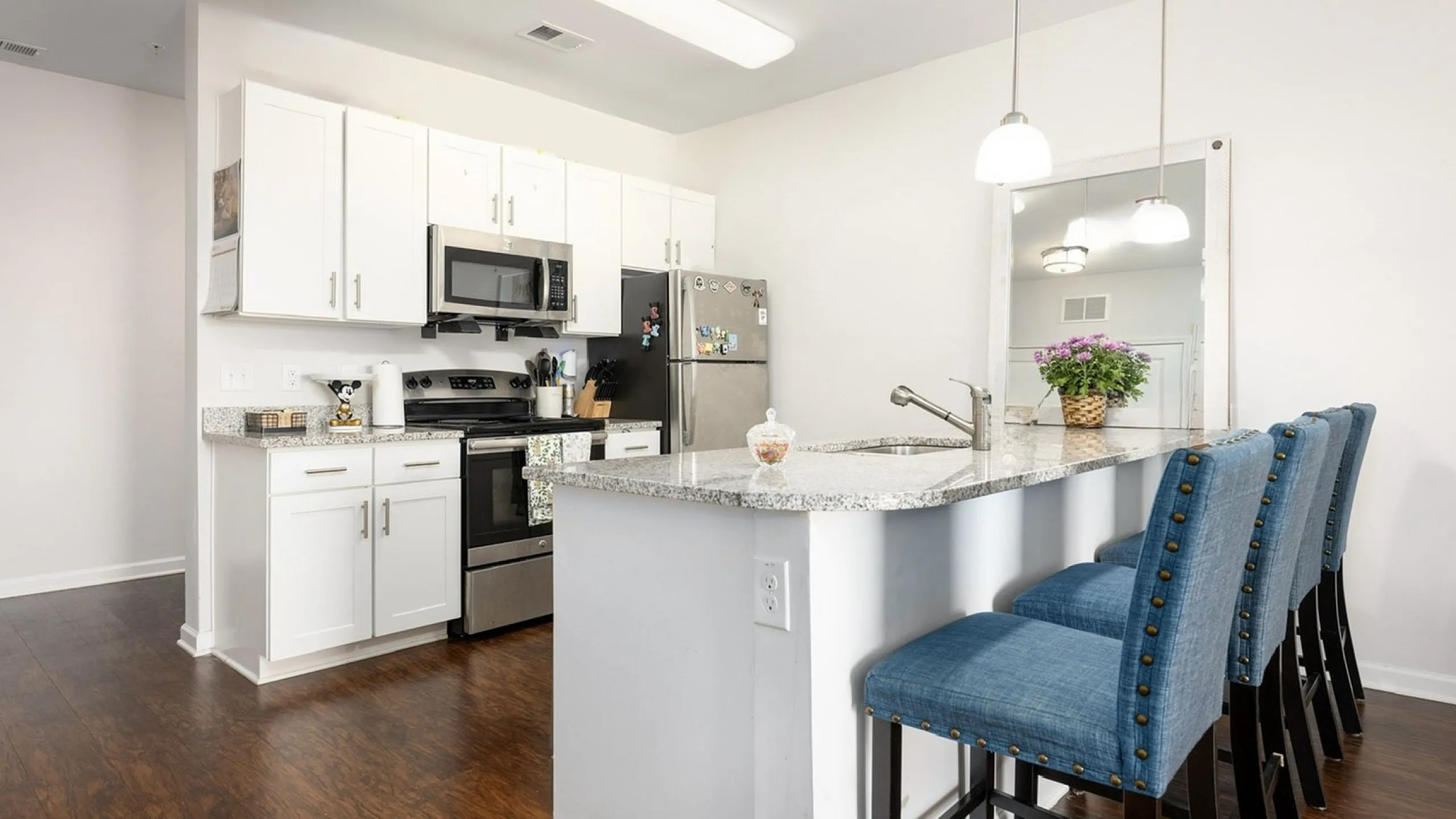 Modern kitchen space with sleek granite countertops, stainless steel appliances, and cozy blue bar stools under elegant pendant lighting.