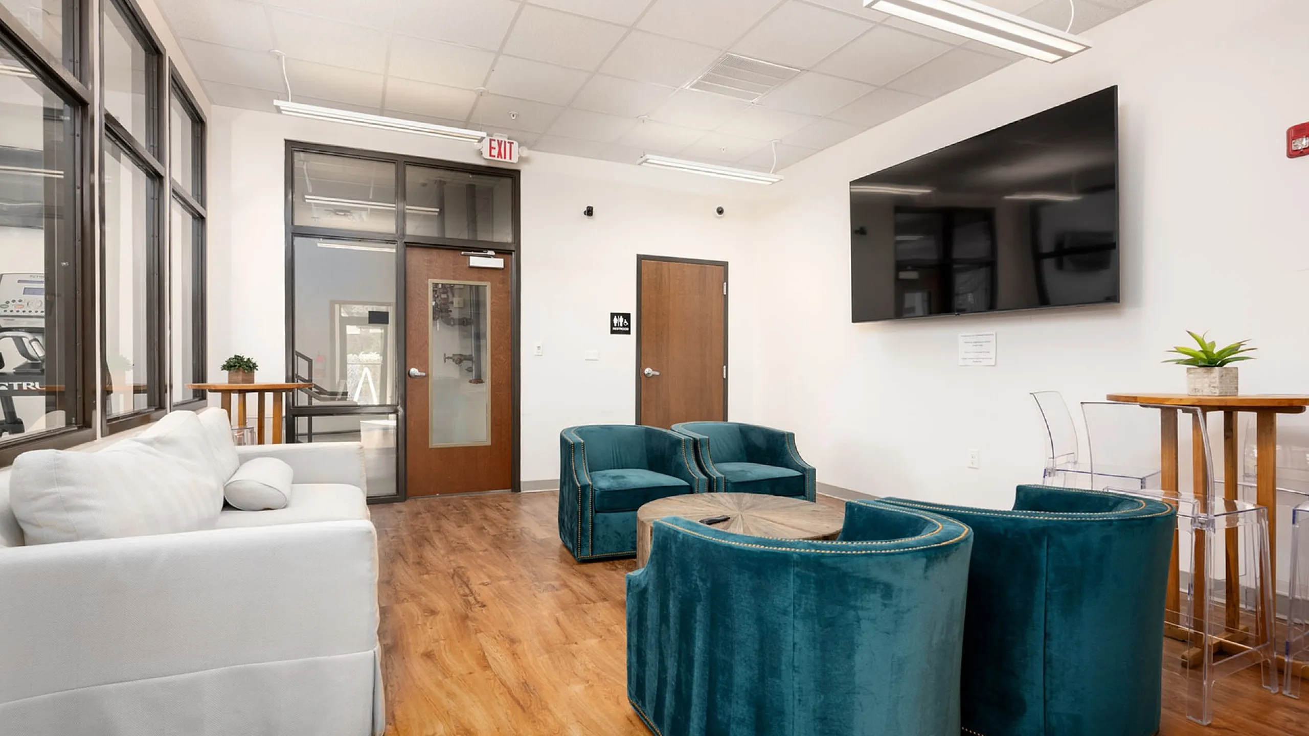 Inviting lounge area featuring plush teal chairs, a sleek white sofa, and modern decor, perfect for relaxation and socializing.