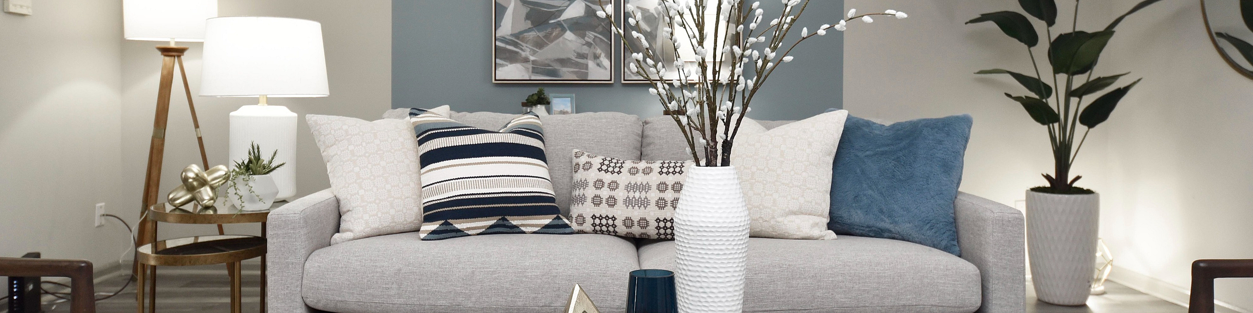 Elegant living room with a modern gray sofa, stylish cushions, and chic decor elements, beautifully lit by contemporary lamps and complemented by green plants.