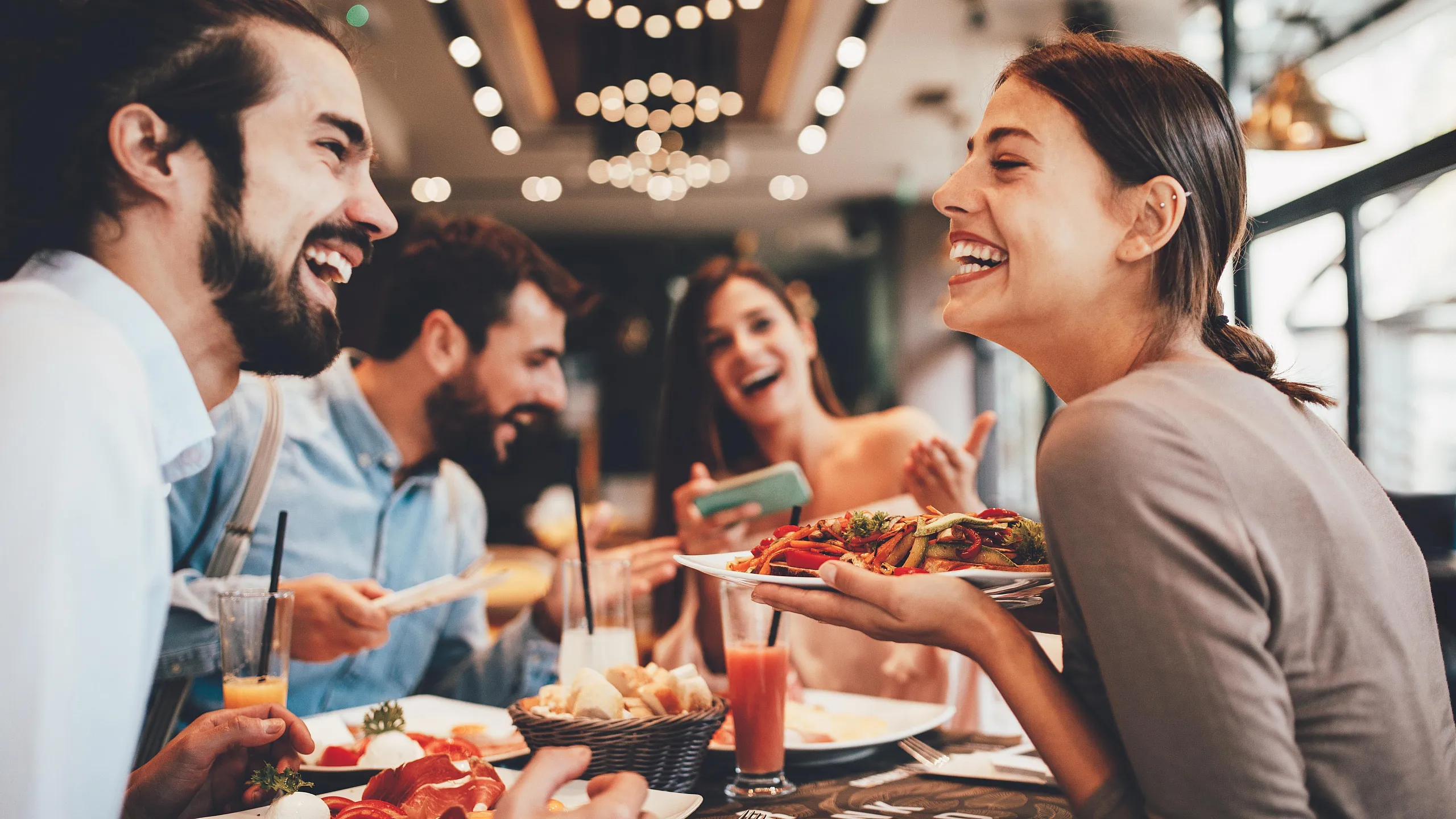 Joyful group of friends enjoying a delicious meal and vibrant conversation in a stylish restaurant setting.