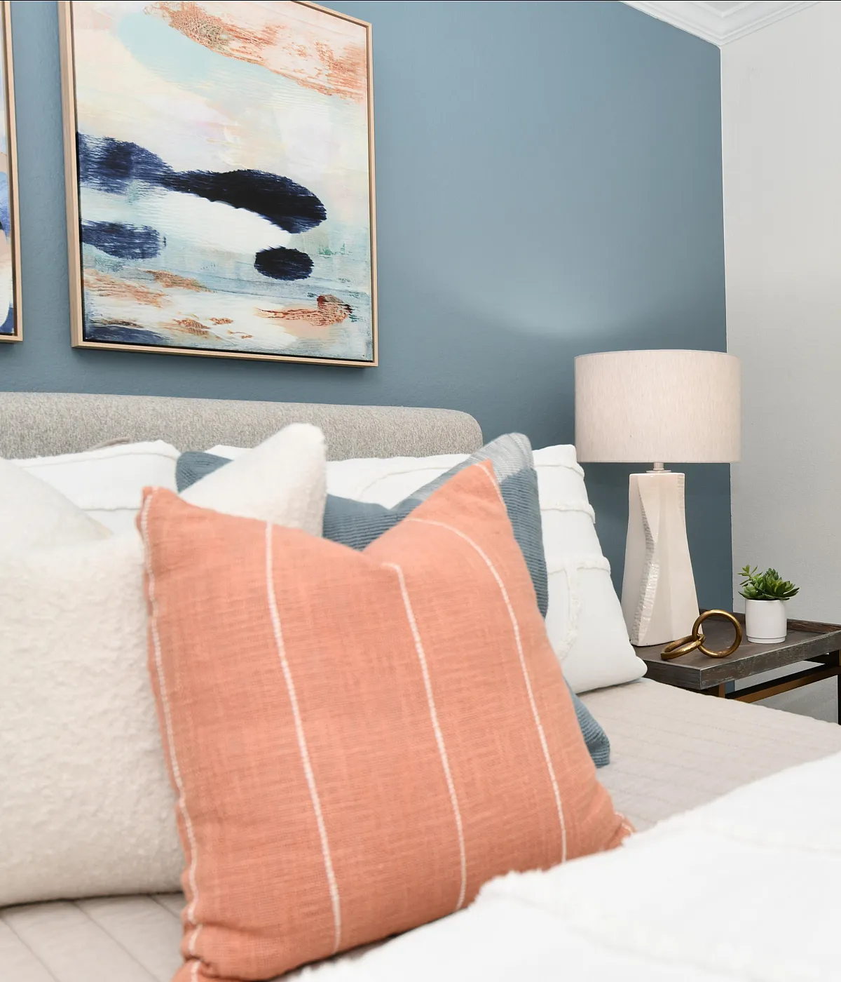 Chic bedroom with stylish abstract art, cozy pillows, elegant lamp, and scenic window view.