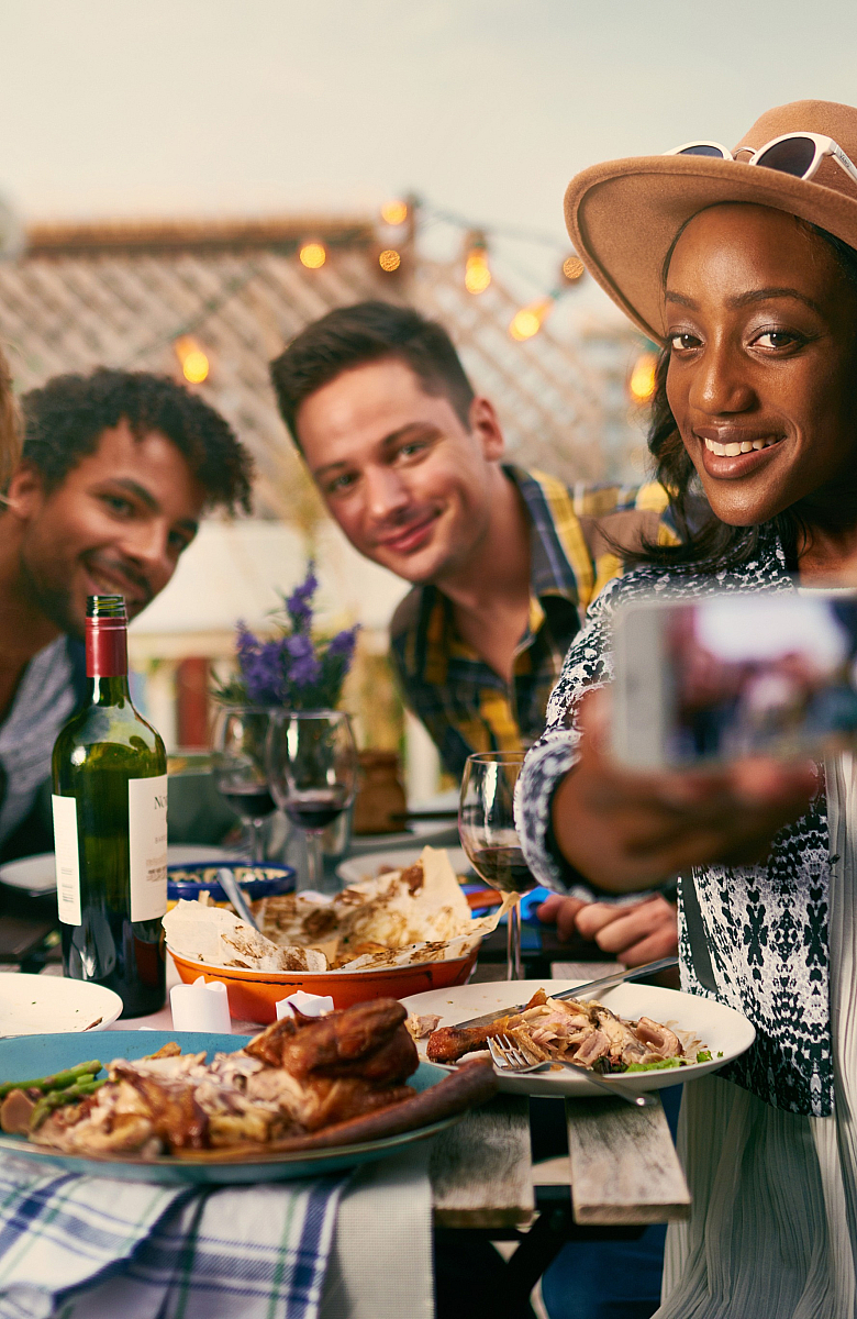 Joyful group of friends enjoying dinner on a beautifully decorated rooftop patio, capturing the moment with a selfie.