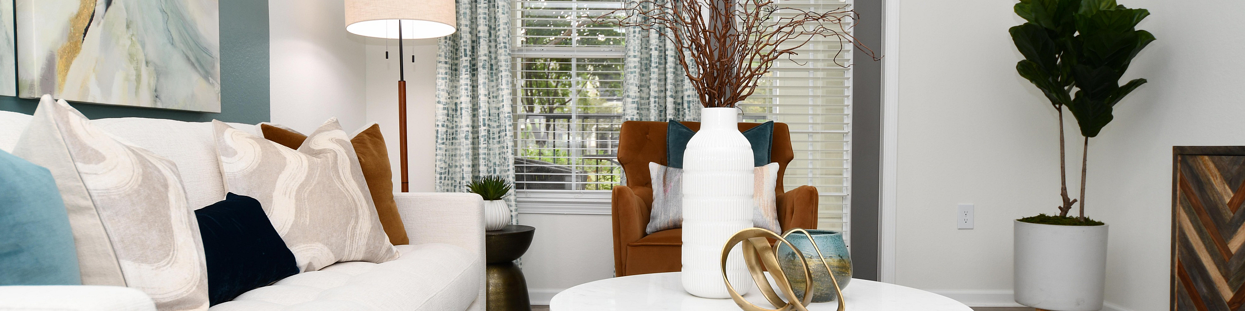 Modern living room with natural light, featuring a plush white sofa, abstract art, and elegant decor.