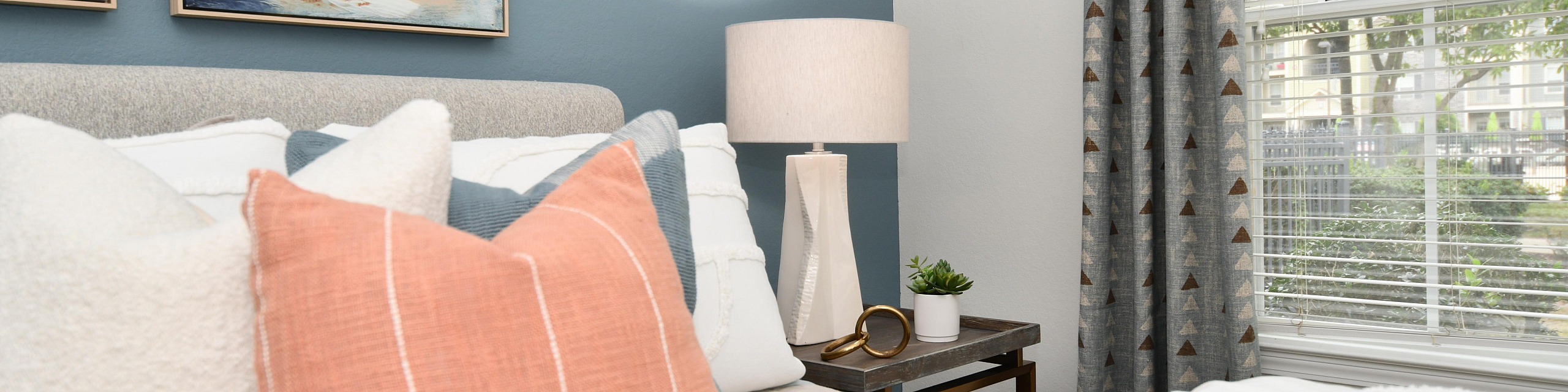 Inviting bedroom with modern decor, plush pillows, abstract wall art, and a large window letting in natural light.