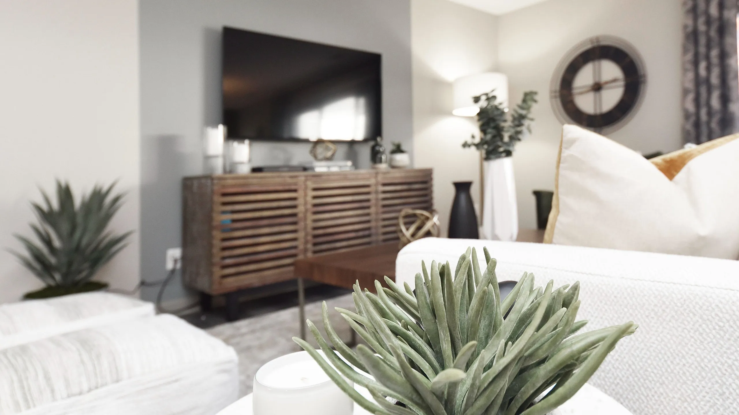 Bright and modern living room with elegant decor, featuring a large TV, cozy seating, and lush indoor plants for a serene atmosphere.