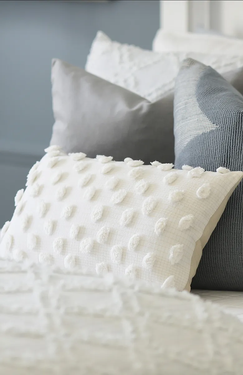 Elegant bedroom decor with a mix of textured pillows in soft gray and white tones, creating a cozy and inviting atmosphere.