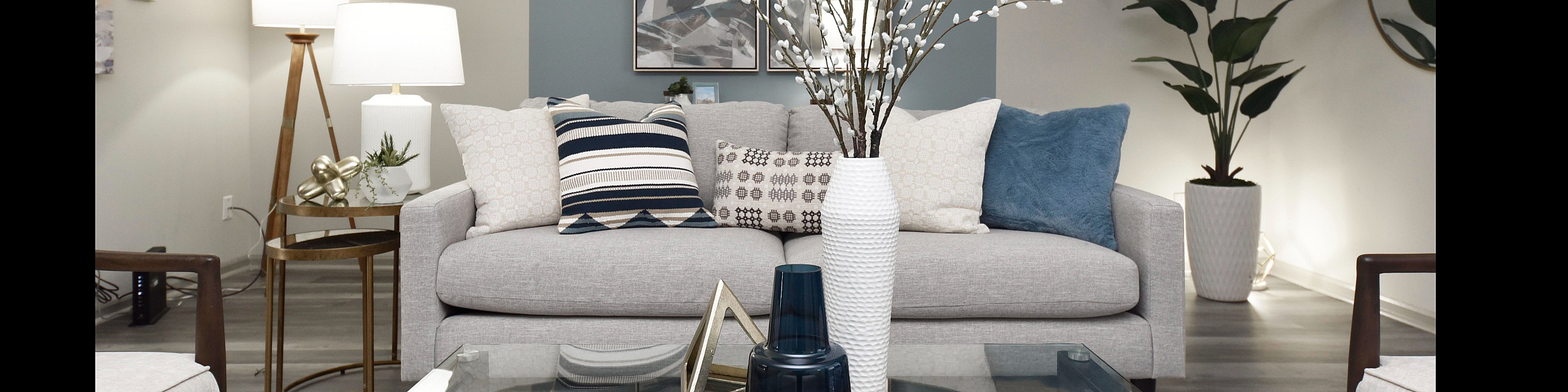 Elegant living room featuring a modern gray sofa with decorative pillows, a sleek glass coffee table, and vibrant plants enhancing the tranquil atmosphere.