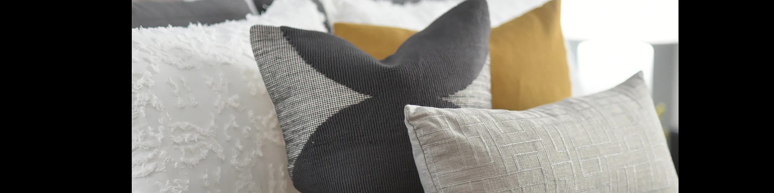 Elegant arrangement of textured pillows in various fabrics and colors on a cozy bed, radiating a modern and stylish bedroom aesthetic.