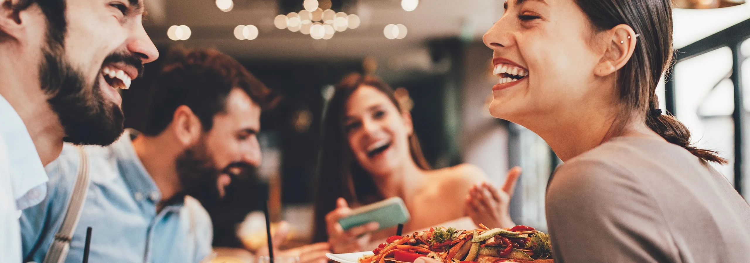 Vibrant group of friends sharing a joyful meal in a lively restaurant setting, filled with laughter and delicious dishes.