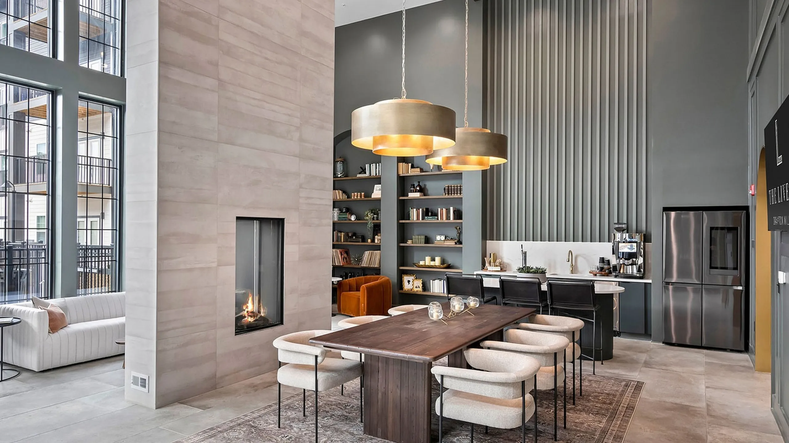 Luxurious apartment interior featuring a modern dining area with elegant pendant lighting, a sleek kitchen with bar seating, and a cozy fireplace, all framed by floor-to-ceiling windows.