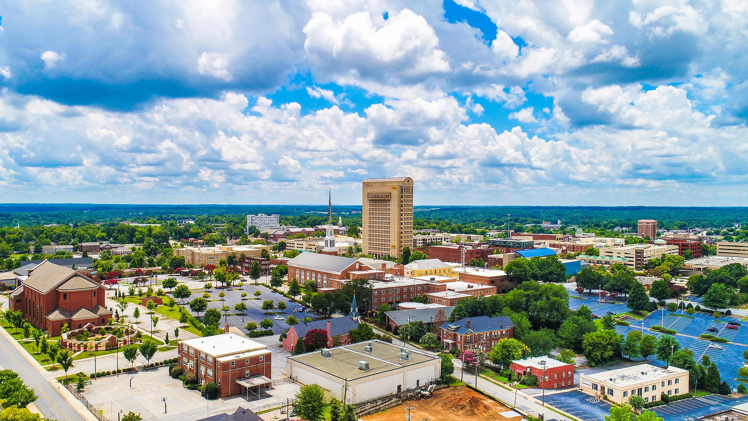 Vibrant aerial view capturing a scenic landscape with a mix of historic and modern architecture, surrounded by lush greenery under a bright blue sky.