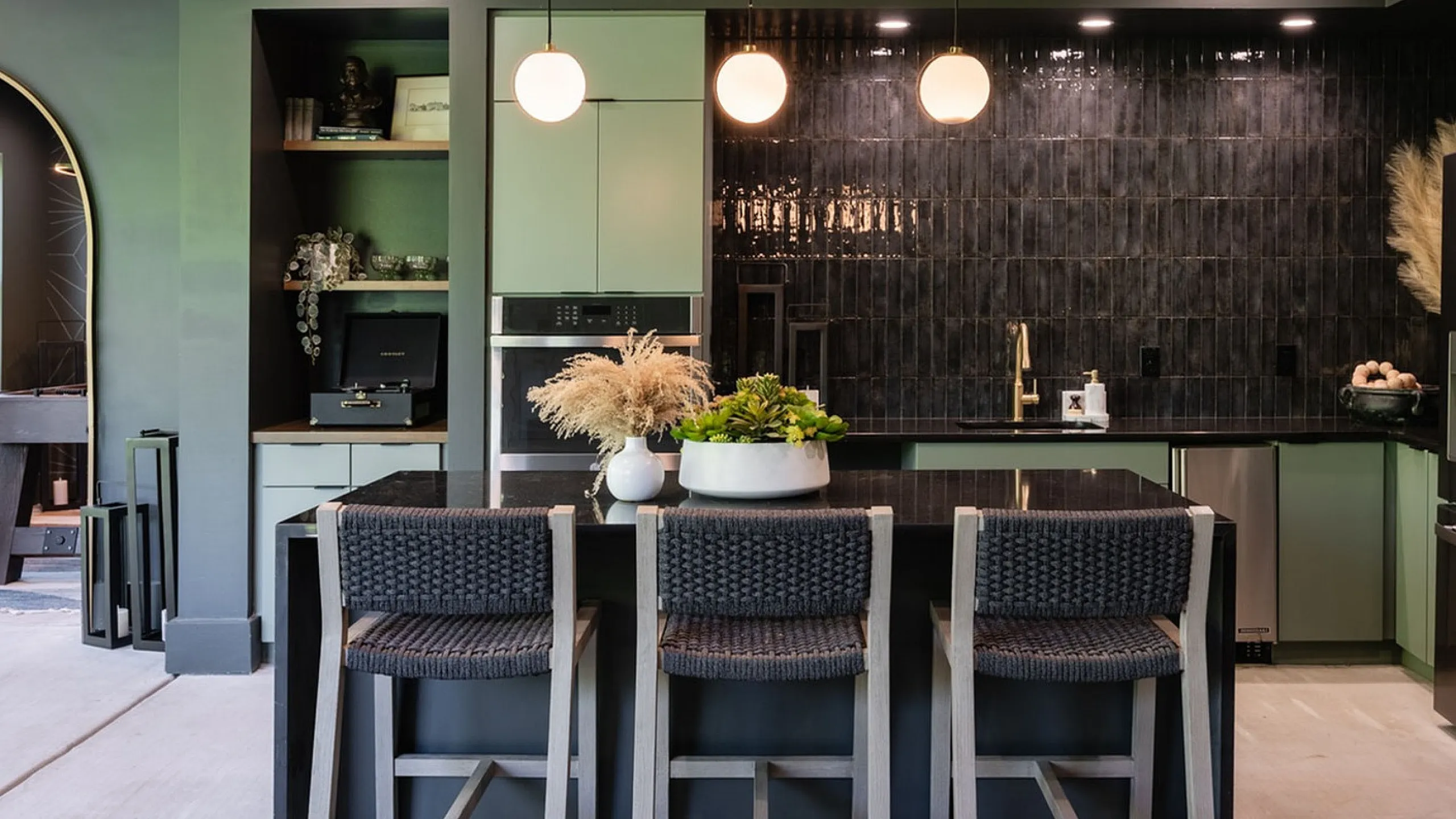 Elegant open-concept kitchen and dining area featuring modern lighting, chic bar seating, and lush indoor greenery, perfect for stylish entertaining.