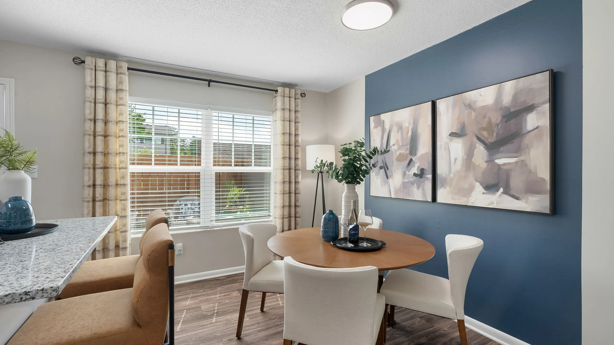 Chic dining area with elegant round table, modern artwork, and abundant natural light overlooking a lush garden.