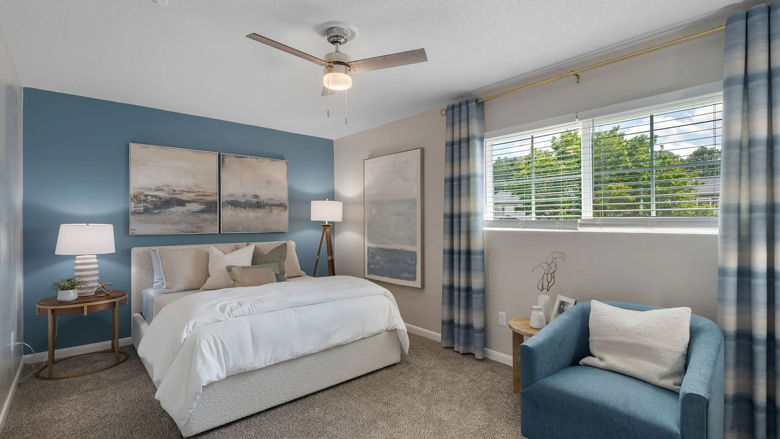 Inviting bedroom with modern decor, featuring a cozy bed, stylish blue accent wall, and a comfortable armchair near a large window allowing natural light.