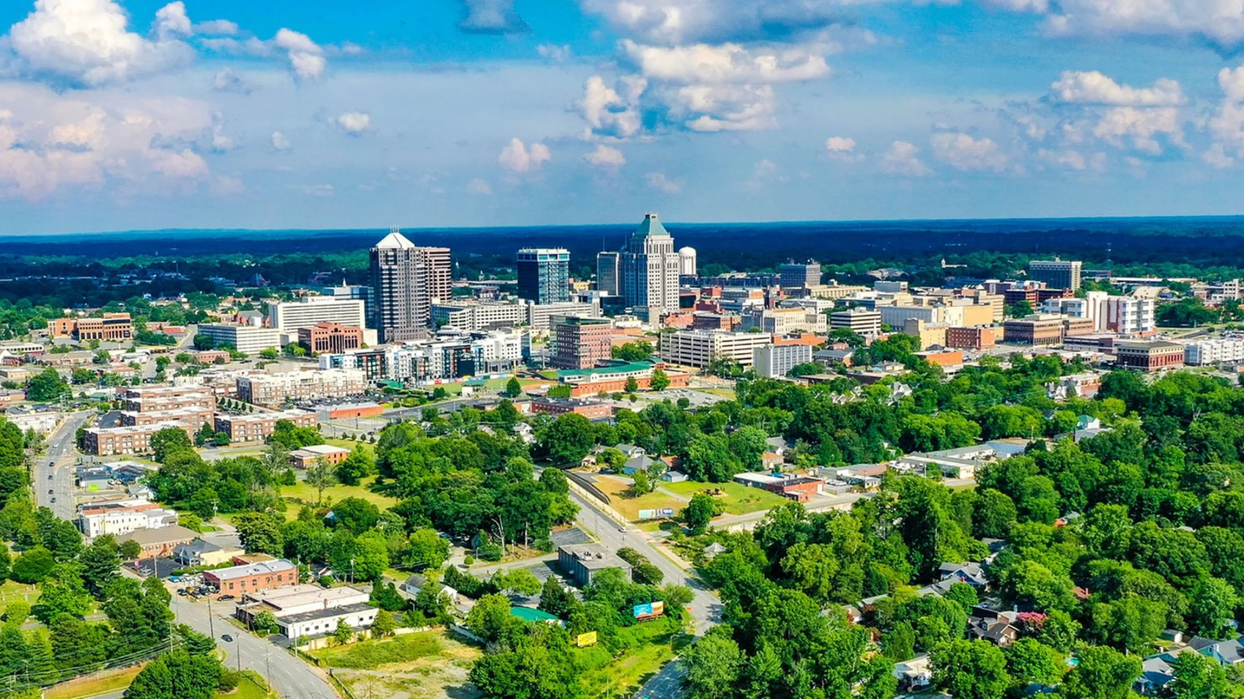 Vibrant aerial view of a lush, green cityscape with modern high-rise buildings under a bright blue sky, showcasing urban living at its best.