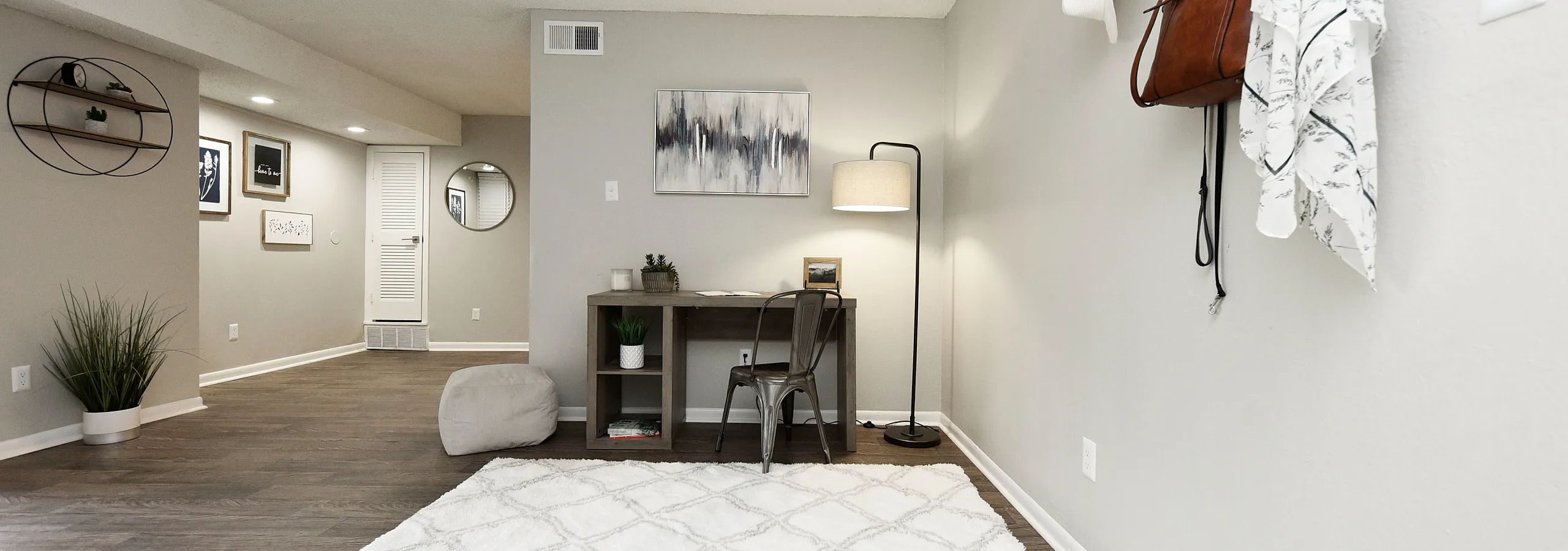 Modern apartment with chic workspace featuring stylish desk, cozy lamp, and elegant decor on warm wooden floors.
