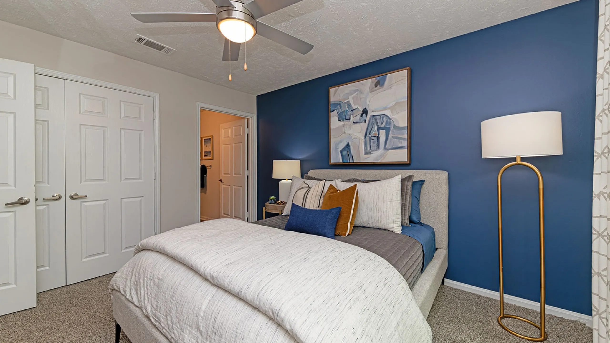 Modern bedroom featuring a comfortable bed, elegant blue accent wall, and sleek ceiling fan, exuding a cozy and stylish ambiance.