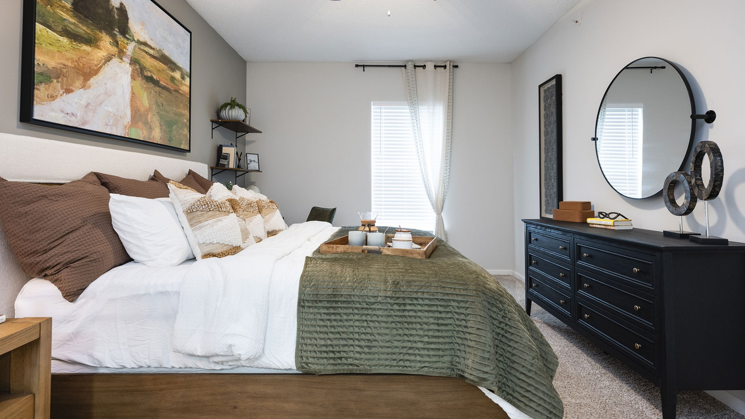 Sophisticated bedroom featuring a cozy bed with plush pillows, stylish artwork, modern decor, and a sleek black dresser under soft natural light.