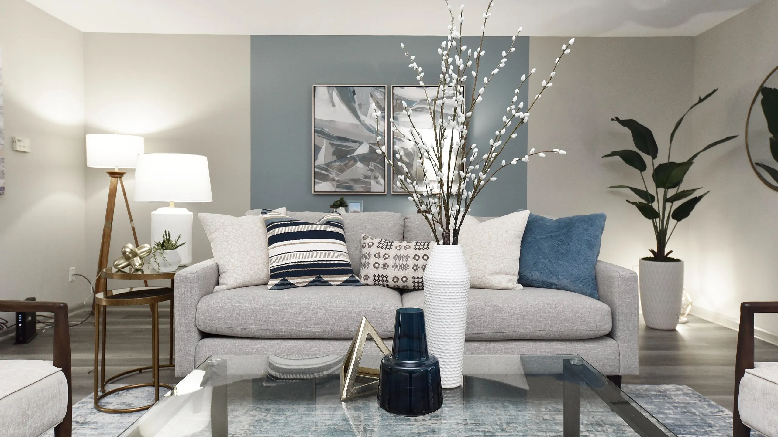 Inviting living room with modern decor, featuring a cozy gray sofa and stylish blue accents, complemented by elegant vases and lush indoor plants.