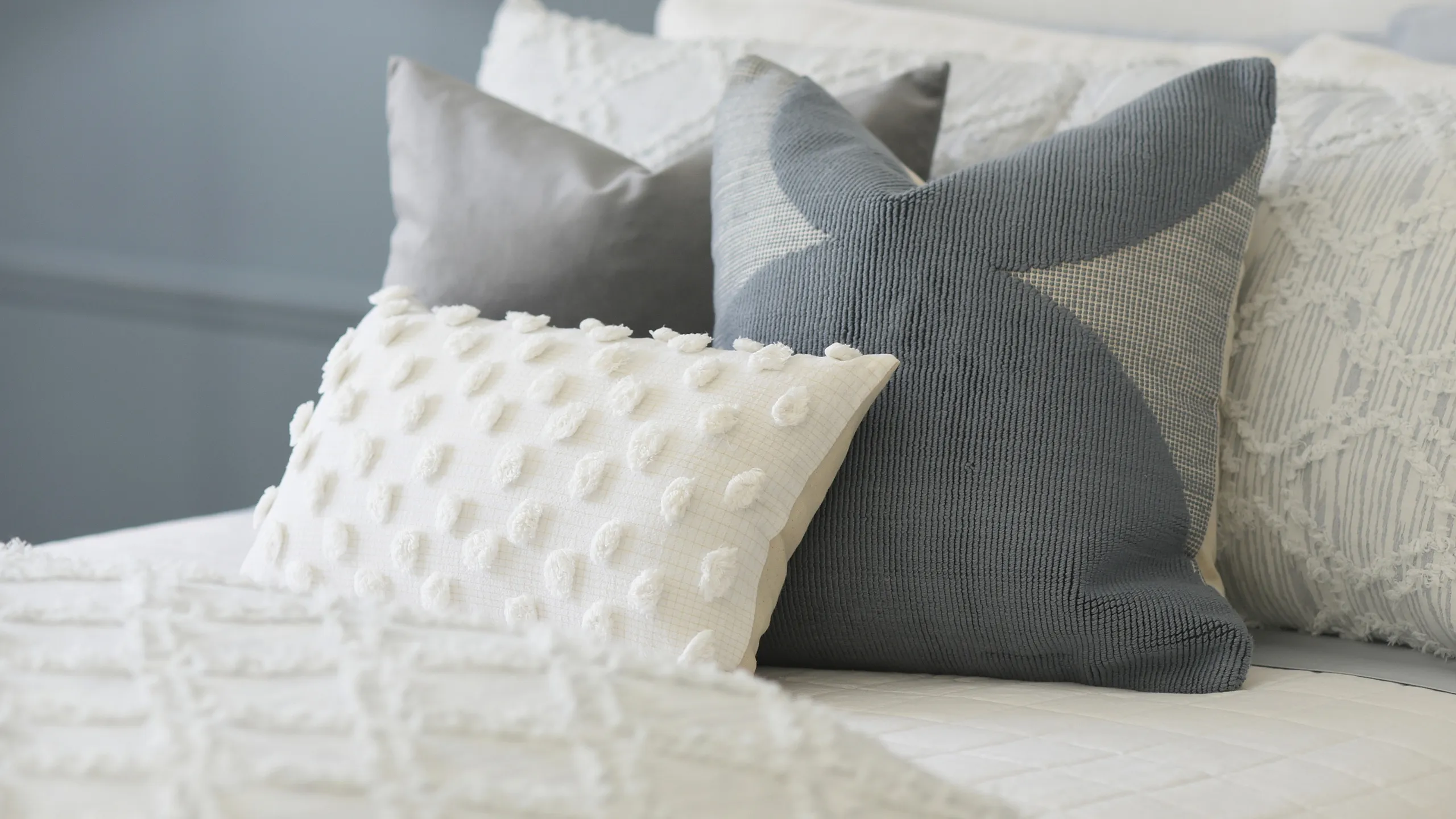 Inviting bedroom with elegant textured pillows and a luxurious white comforter, creating a serene and cozy ambiance.