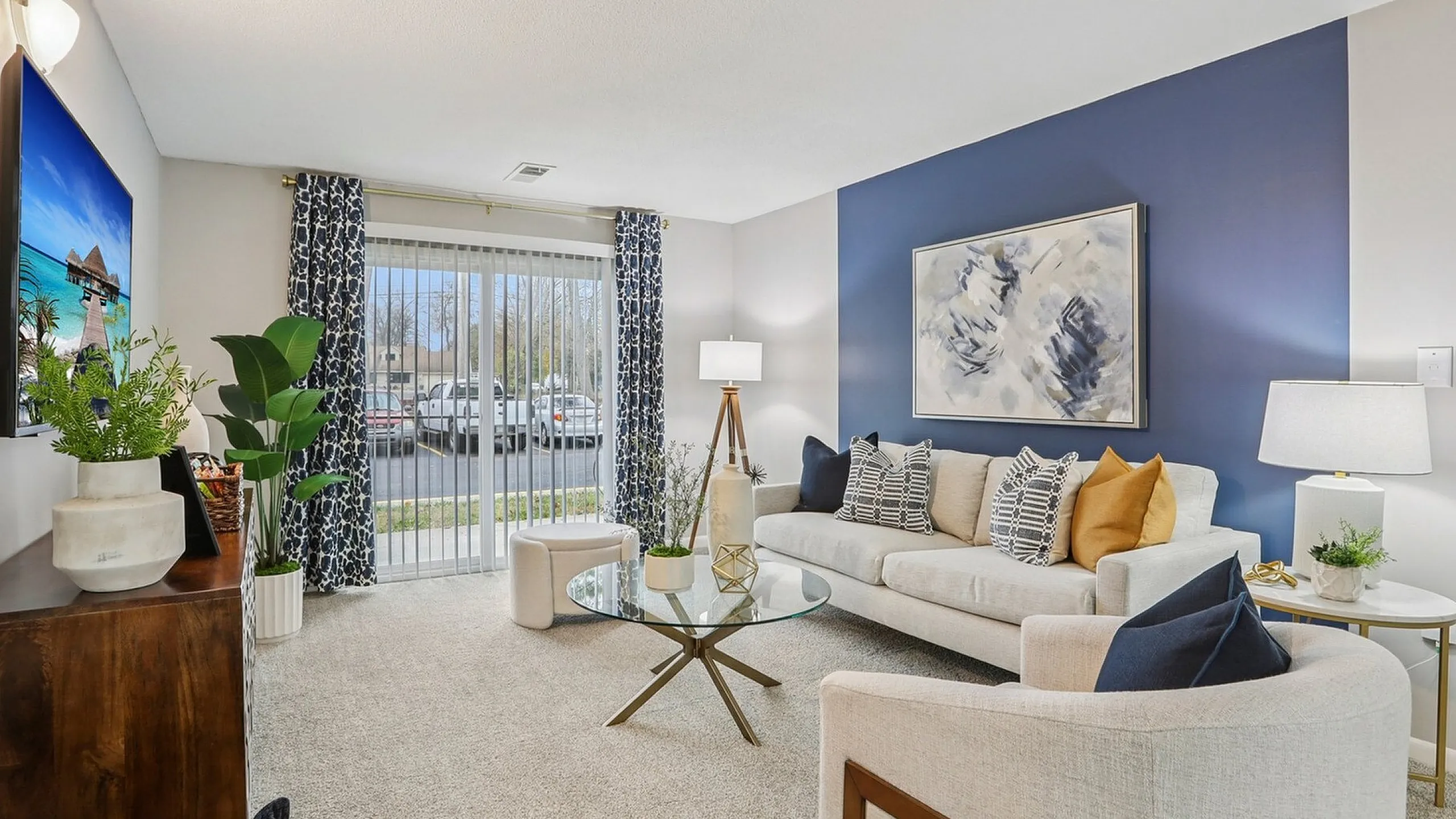 Contemporary living room with elegant blue accent wall, cozy beige sofa adorned with stylish cushions, glass coffee table, and modern decor, bathed in natural light from floor-to-ceiling windows.