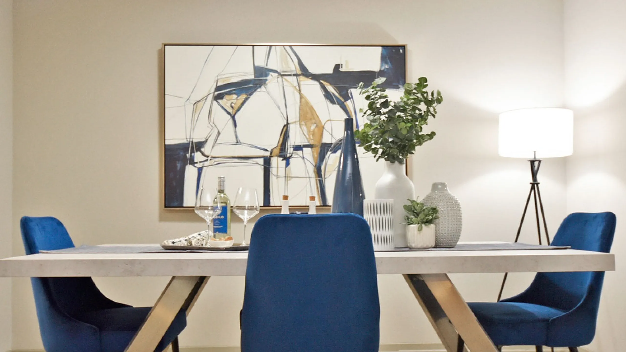Elegant dining area featuring a modern table with vibrant blue chairs, sophisticated abstract artwork, and stylish decor accents.