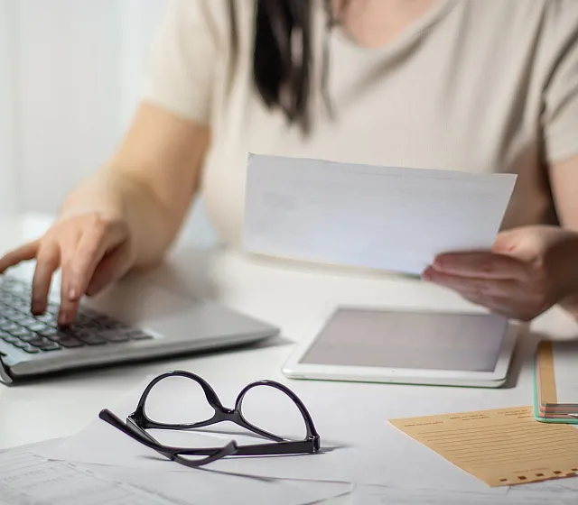 Professional workspace ambiance with a person engaging in paperwork and using a laptop, emphasizing productivity and organization.